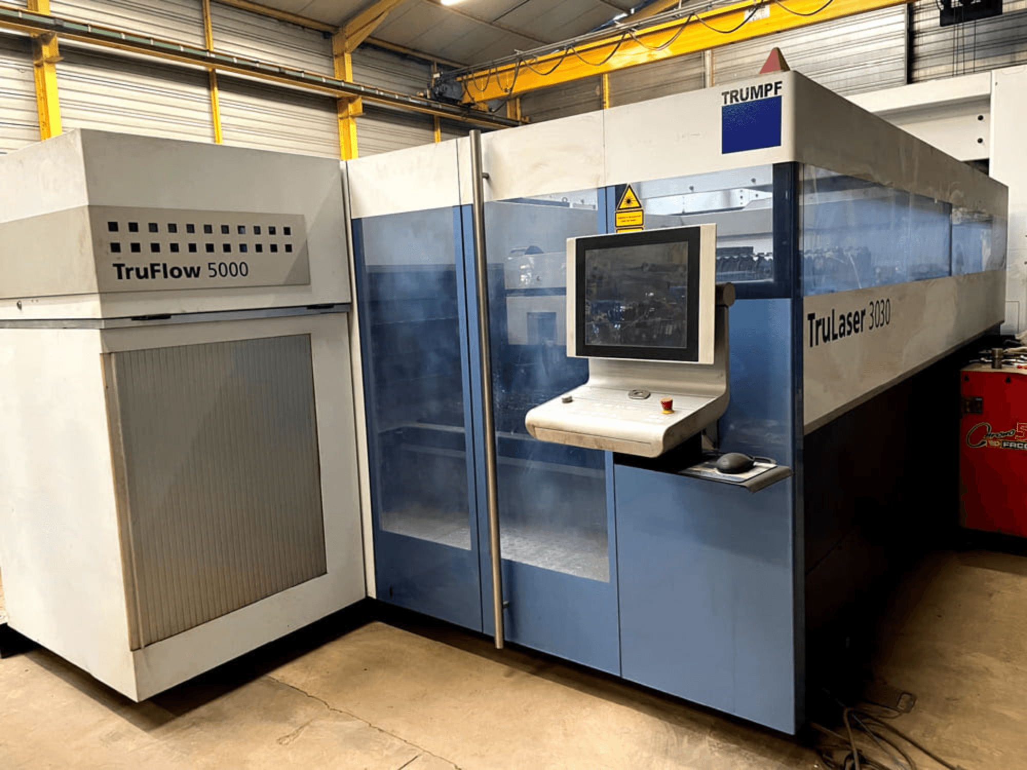 TRUMPF TruLaser 3030 CO₂ lazer kesim makinesinin önden görünümü; kontrol paneli ve yanında yer alan TruFlow 5000 ünitesi ile birlikte.