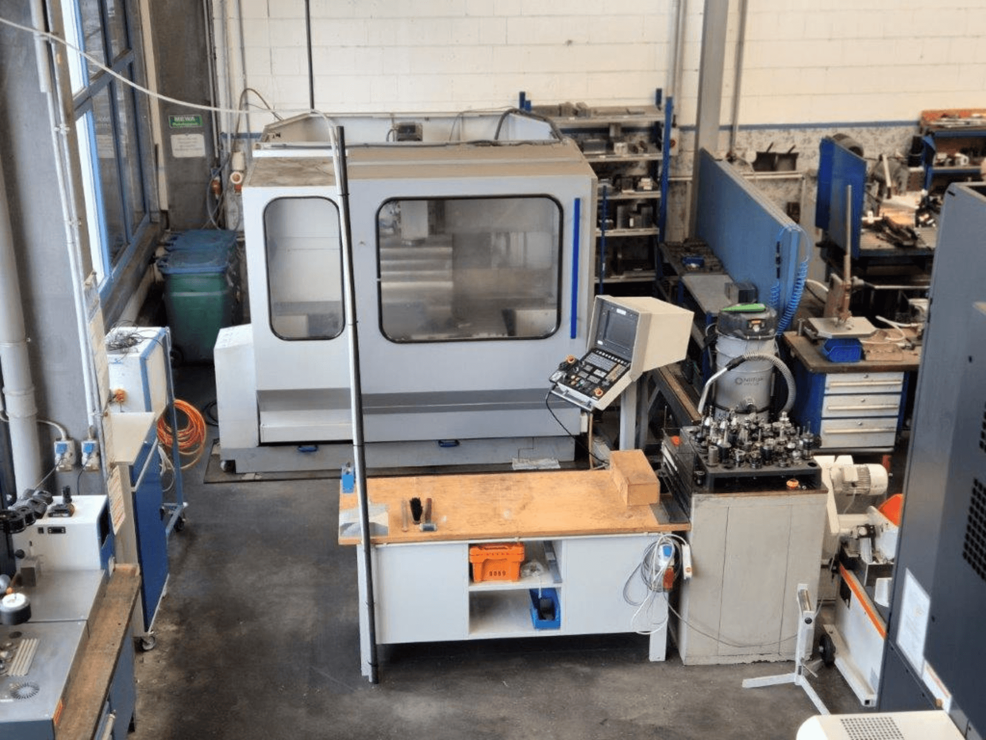 Bir atölyede CNC freze makinesi, önden görünüm, kontrol paneli, çalışma yüzeyi ve arka planda görünen aletler.