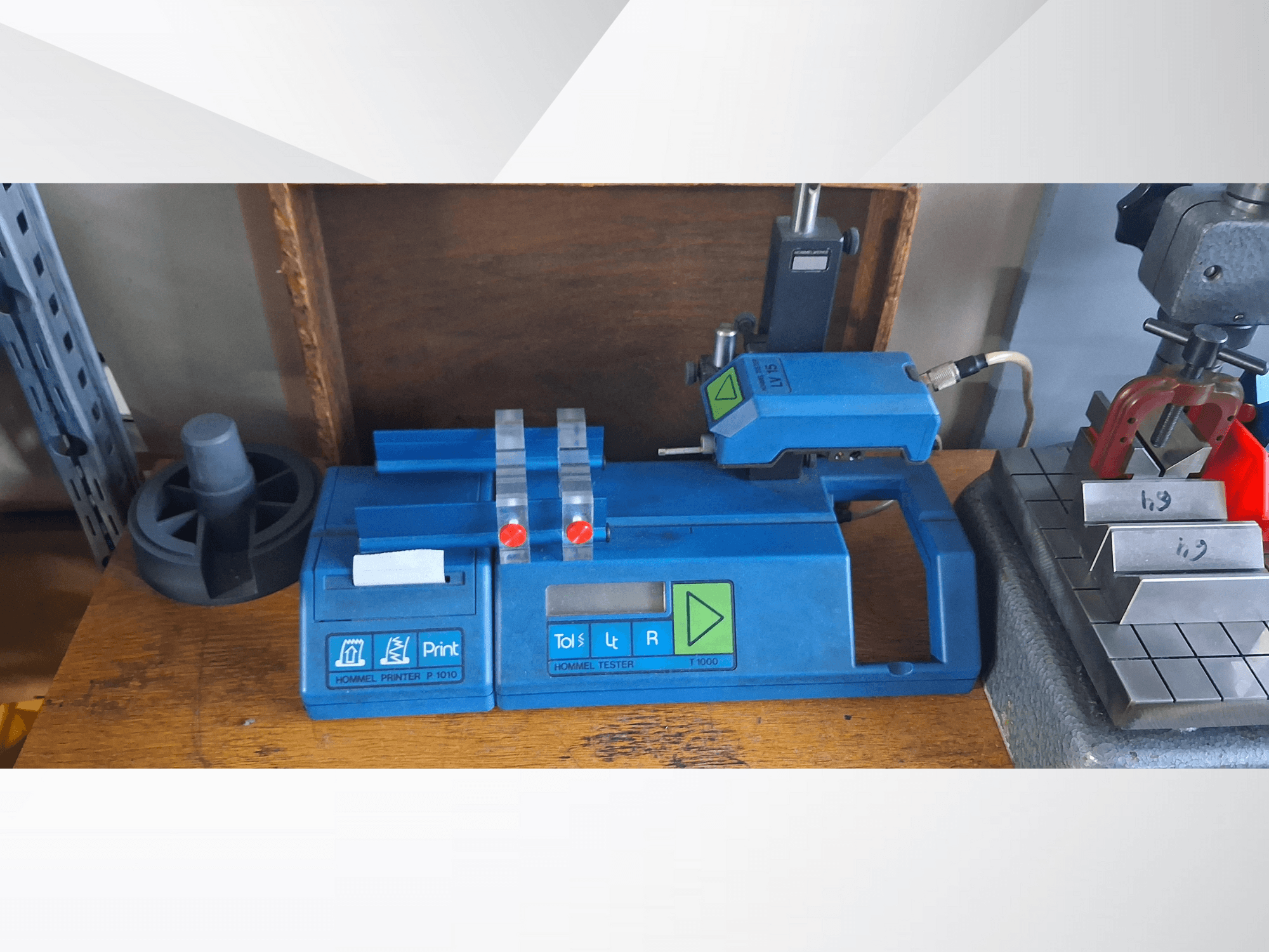 Hommel Printer P 1010 ve Tester T1000'in yandan görünümü, mavi gövde, düğmeler ve kırmızı göstergeler, bir çalışma tezgahı üzerinde.