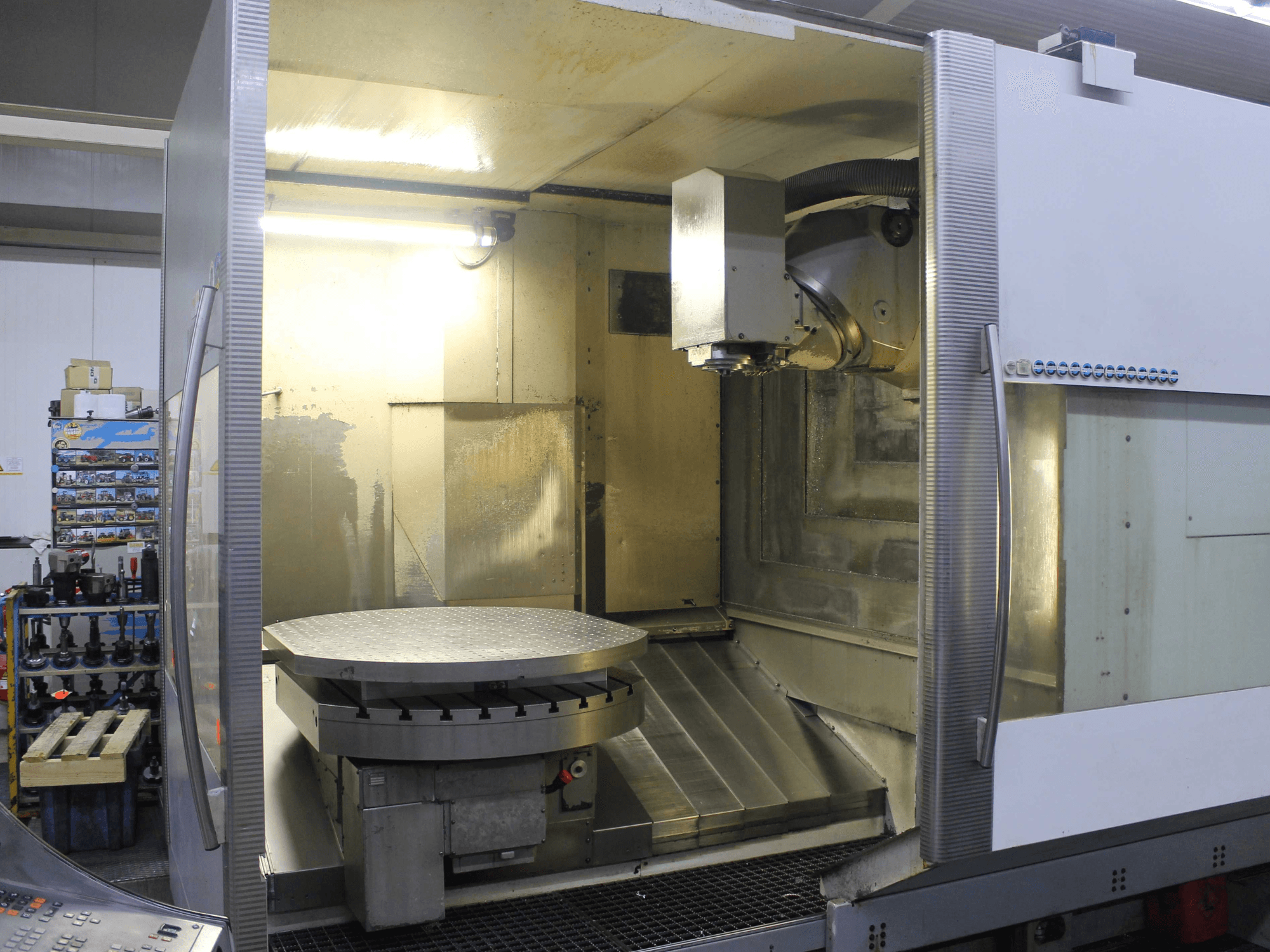 Dairesel döner tablalı ve kesme kafalı CNC freze makinesi, metalik yüzeyler ve aydınlatma ile önden gösterilmiştir.
