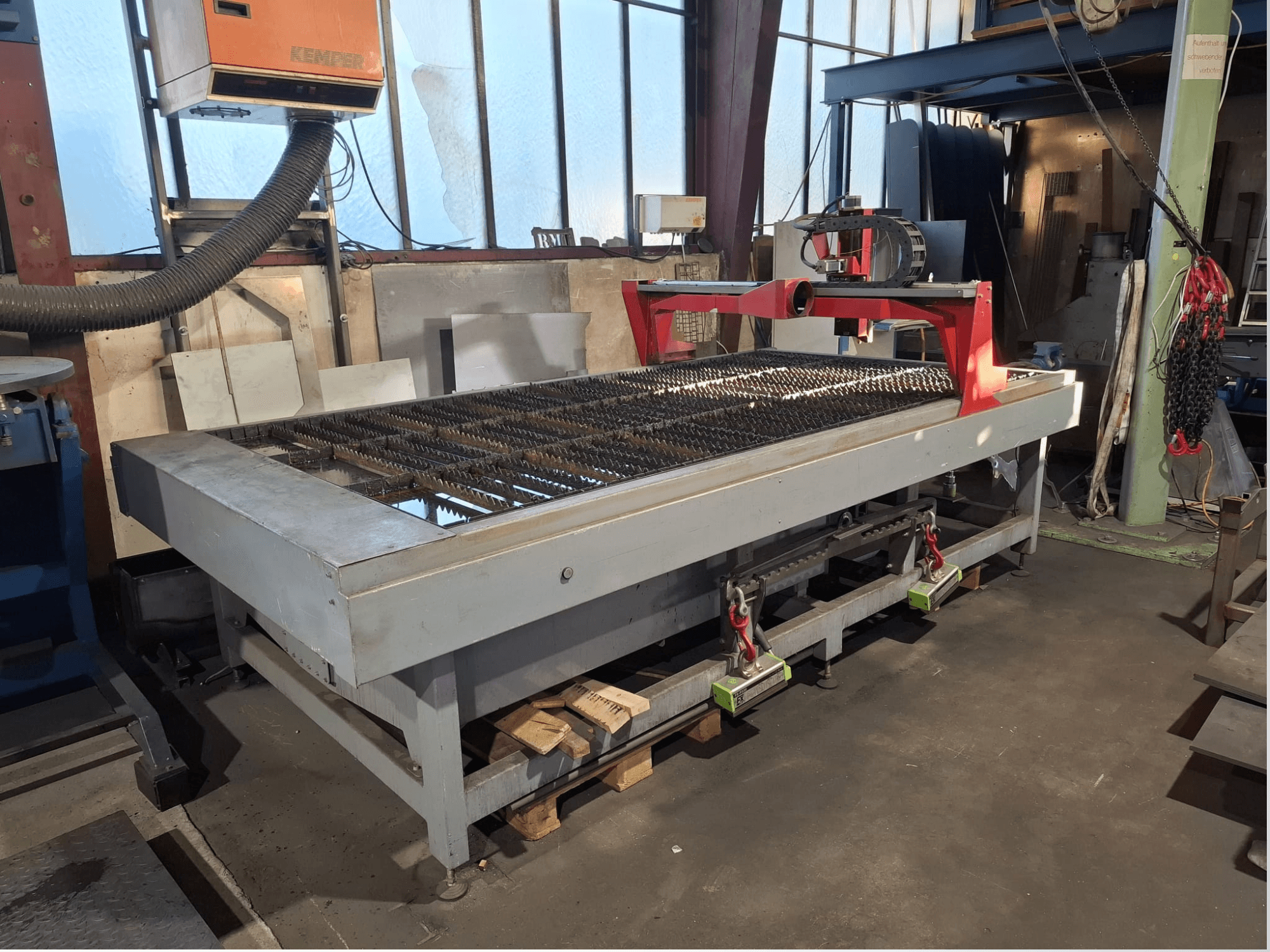 Yan görünümde gösterilen PLASMACUT 3015T plazma kesme makinesi, metal çıtalı geniş bir kesme masası ve kırmızı bir çerçeveye sahiptir.