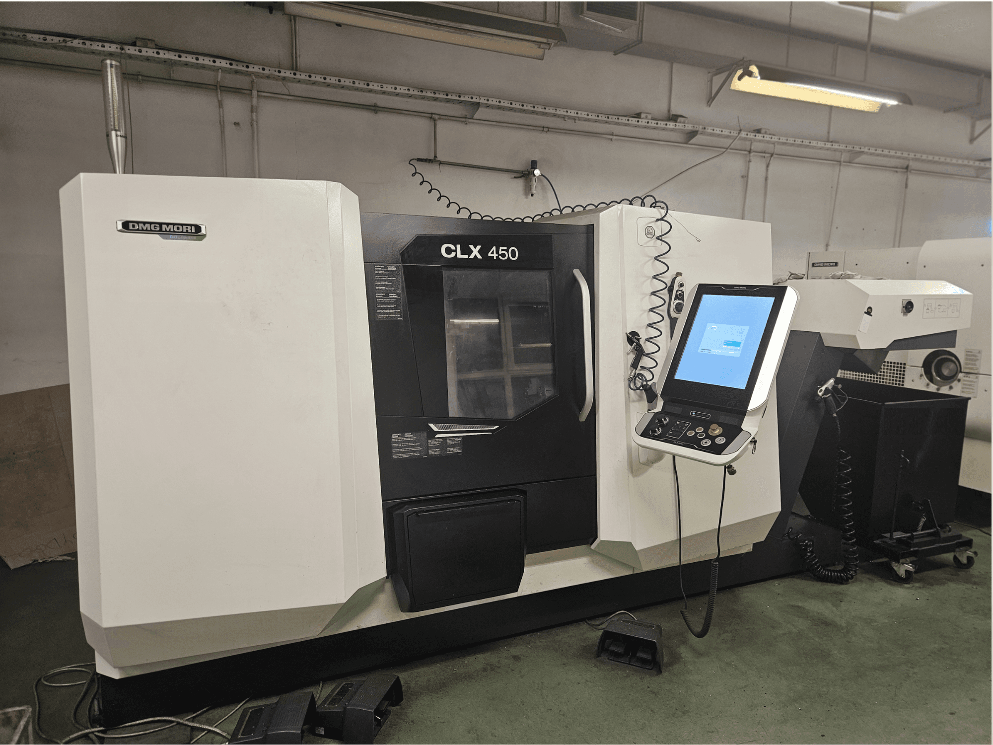 DMG MORI CLX 450 CNC makinesinin önden görünümü, atölye ortamında bir kontrol paneli ve dokunmatik ekrana sahiptir.