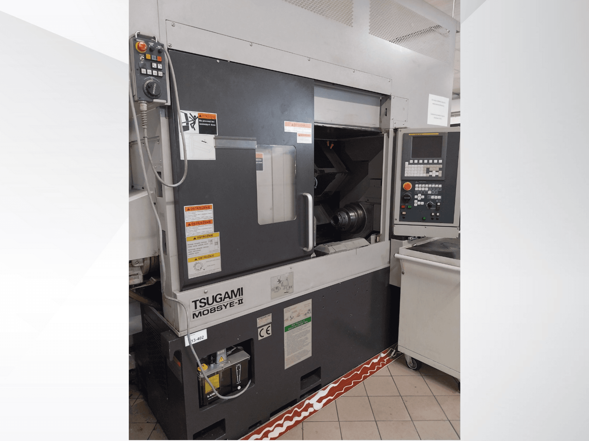 Tsugami M08SY-II CNC torna tezgahı, önden görünüm, kontrol paneli, iş mili ve yükleme alanını gösterir. Güvenlik uyarıları ve marka etiketini içerir.
