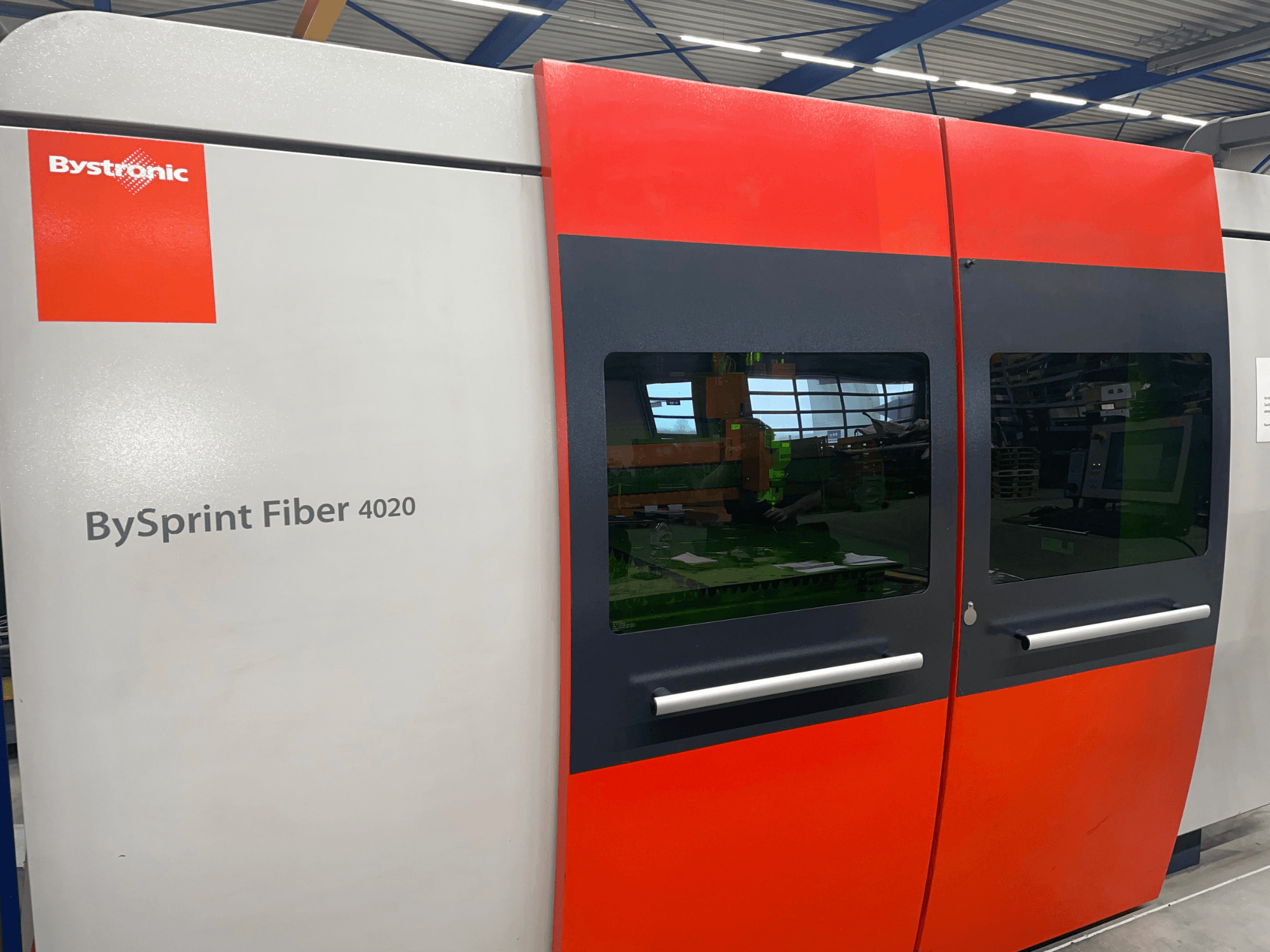 Önden görünümlü Bystronic BySprint Fiber 4020, içinde büyük pencereler ve kontrol arayüzü görünen gri ve kırmızı panel tasarımına sahiptir.