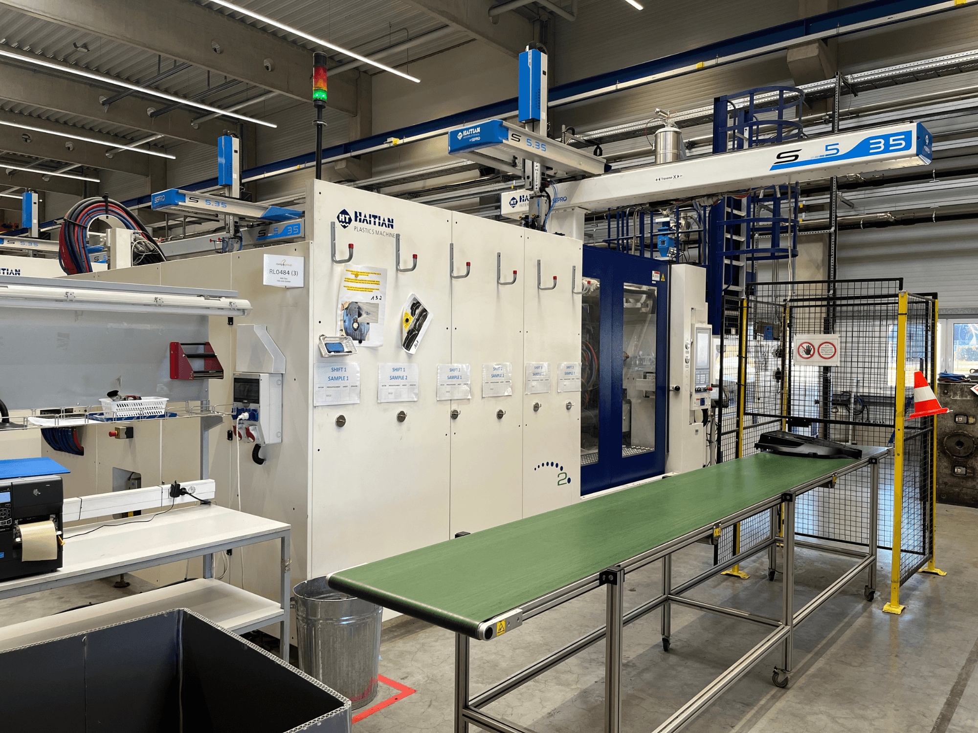 Bir atölyede Haiti S5-35 plastik makinesi; yeşil konveyör tablası, güvenlik bariyerleri ve önden görünen kontrol paneli.
