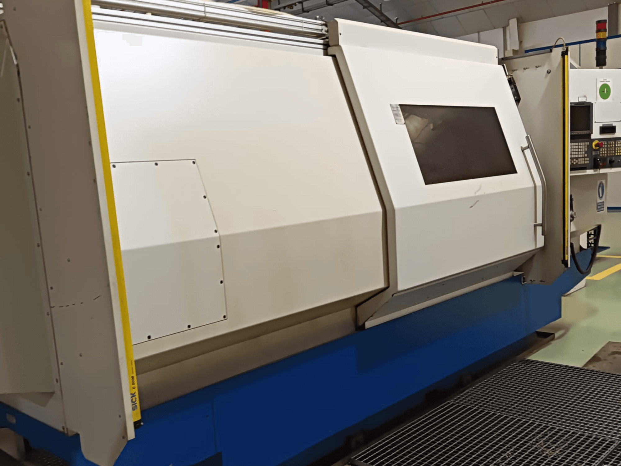 Endüstriyel torna makinesi, yandan görünüm, büyük beyaz ve mavi gövde, dijital kontrol paneli ve güvenlik özellikleri.