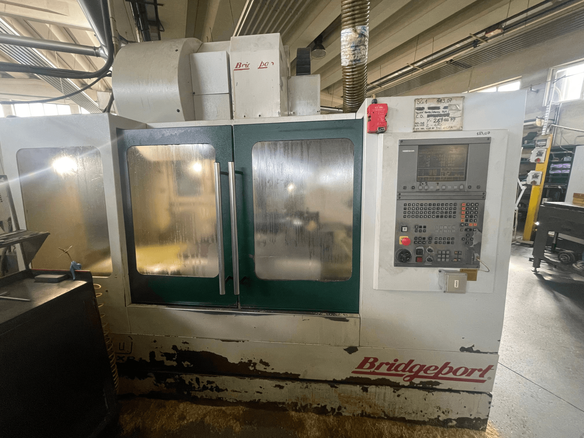 Bridgeport VMC 1000/30 dikey işleme merkezi, kontrol paneli ile birlikte önden görünüm; yıpranmış dış yüzey ve yeşil kapılar görülüyor.