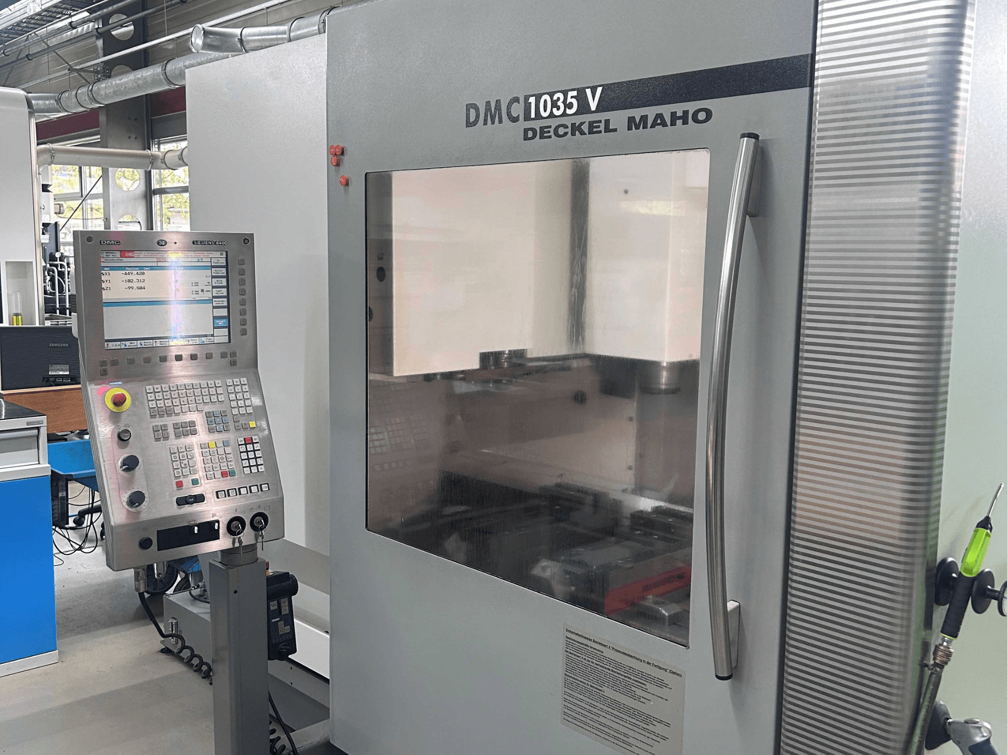 DECKEL MAHO DMC 1035 V dikey işleme merkezinin önden görünümü; kontrol paneli ve çalışma alanına açılan şeffaf pencere görülmektedir.