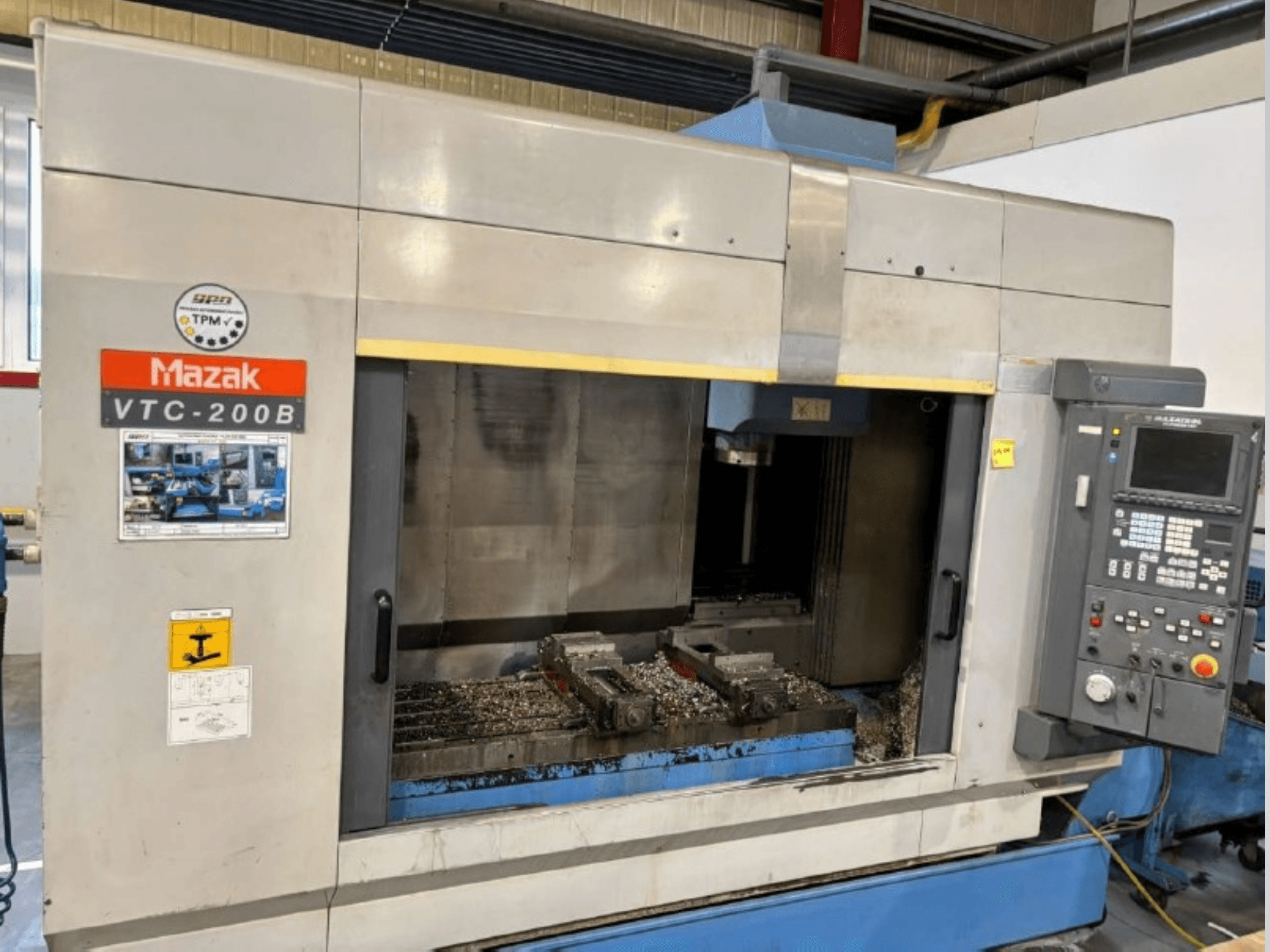 Mazak VTC-200B dikey işleme merkezi, görünür kontrol paneli ve çalışma alanındaki metal talaşları ile yandan görünüm.