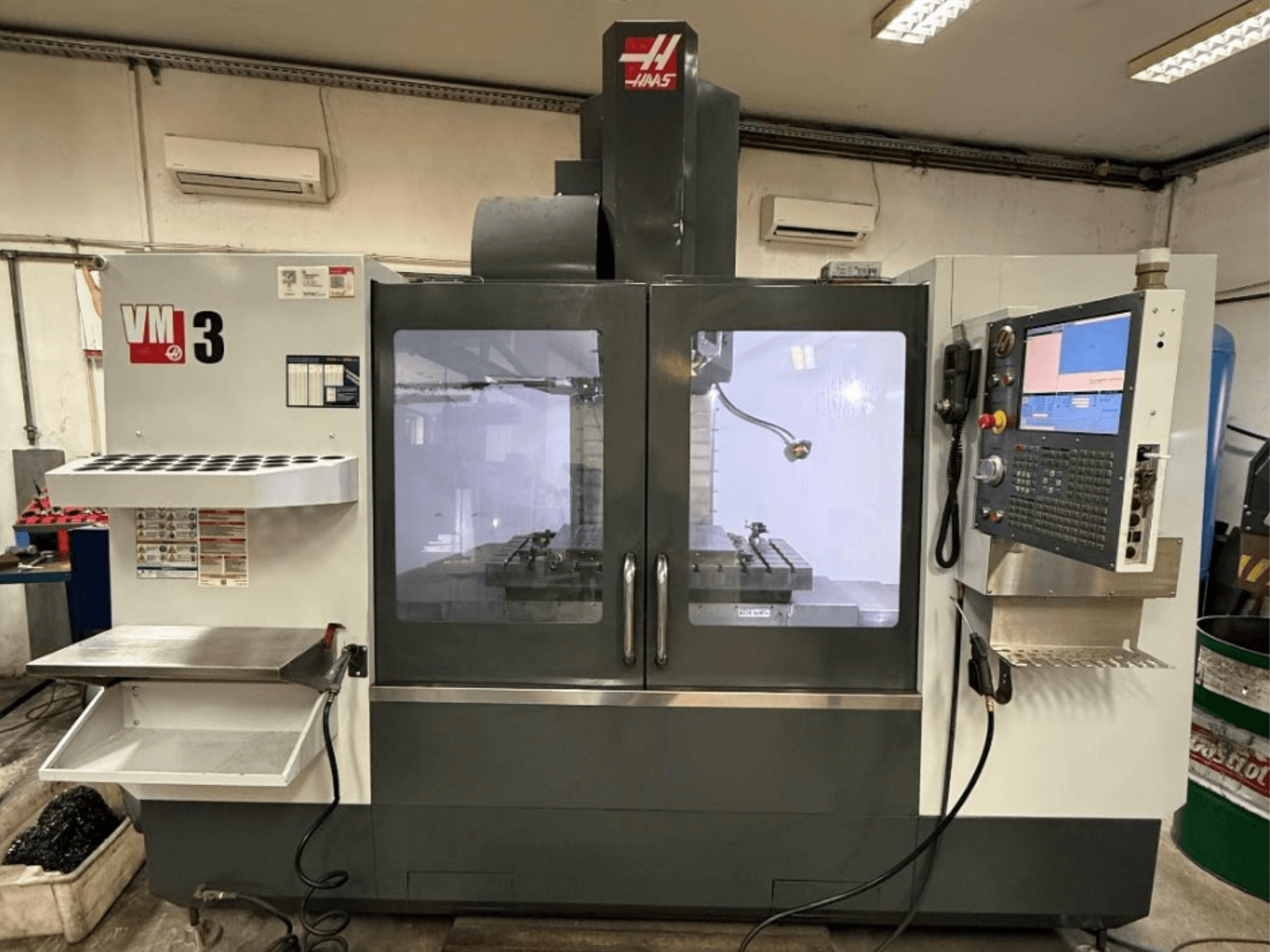 Haas VM-3 dikey işleme merkezinin önden görünümü; geniş bir kontrol paneli ve takımların bulunduğu, açıkça görülebilen işleme alanı ile dikkat çekiyor.