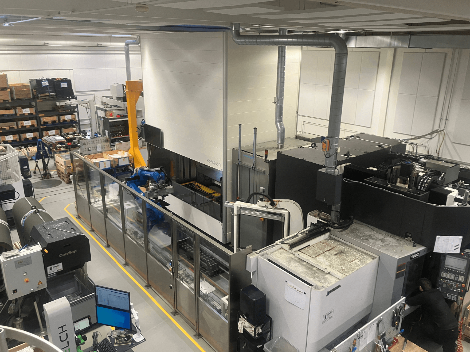 SSI SCHAFER Logimat otomasyon sistemi bir depoda, önden görünüm; robotik kol, depolama rafları ve makinelere sahiptir.