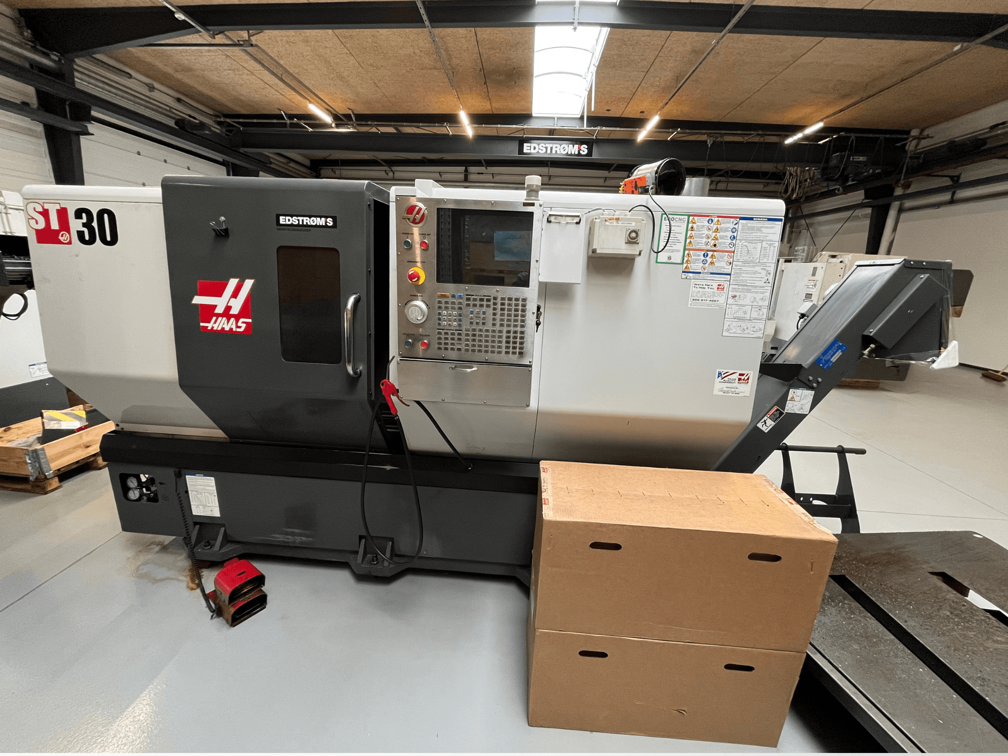 Haas ST-30 CNC torna tezgahına yandan bakıldığında bir kontrol paneli, model rozeti ve yanında iki karton kutu görülüyor.