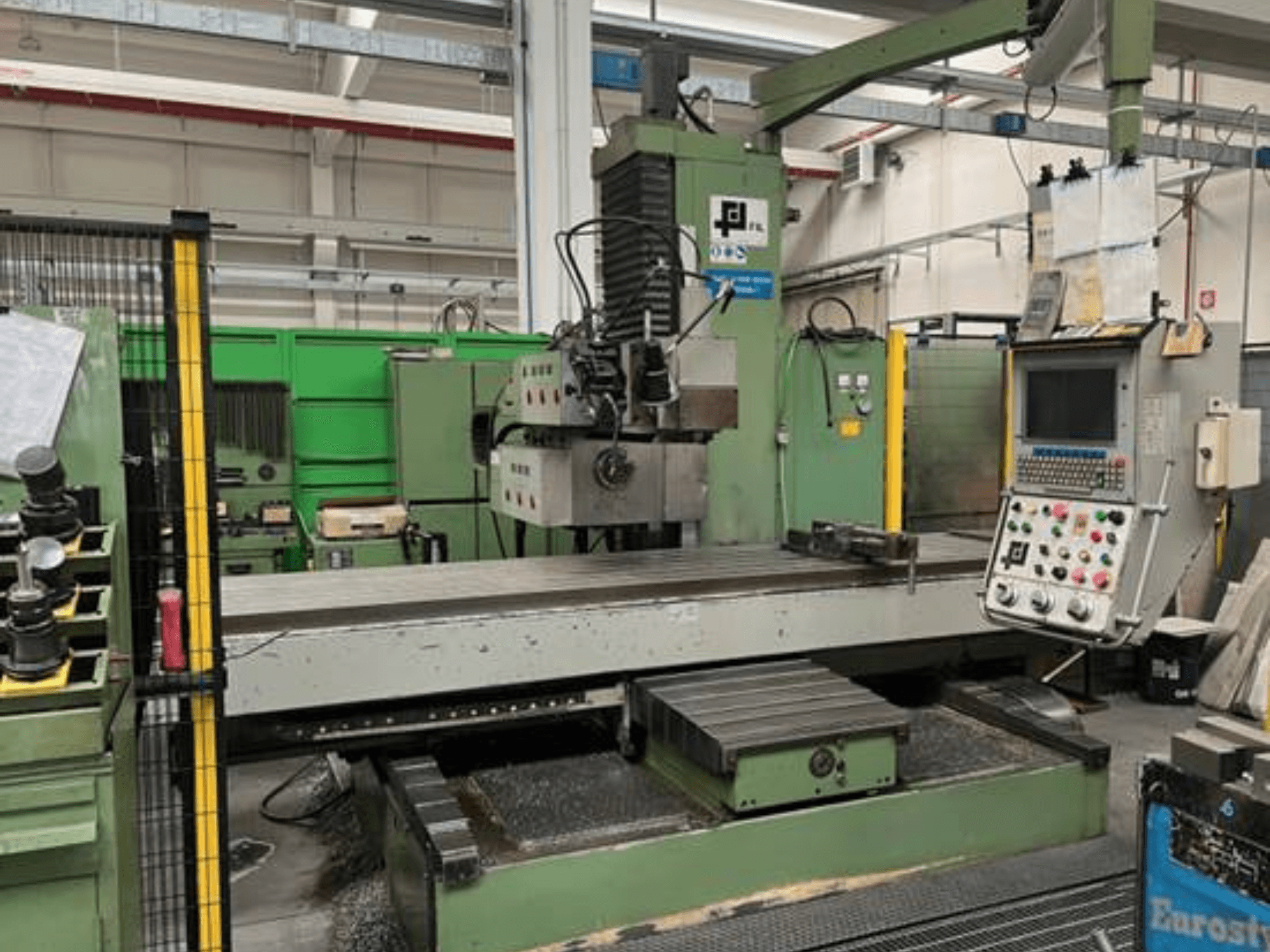 JFL'den endüstriyel freze makinesi, kontrol paneli, büyük düz tabla ve zemindeki metal talaşı ile önden görünüm.