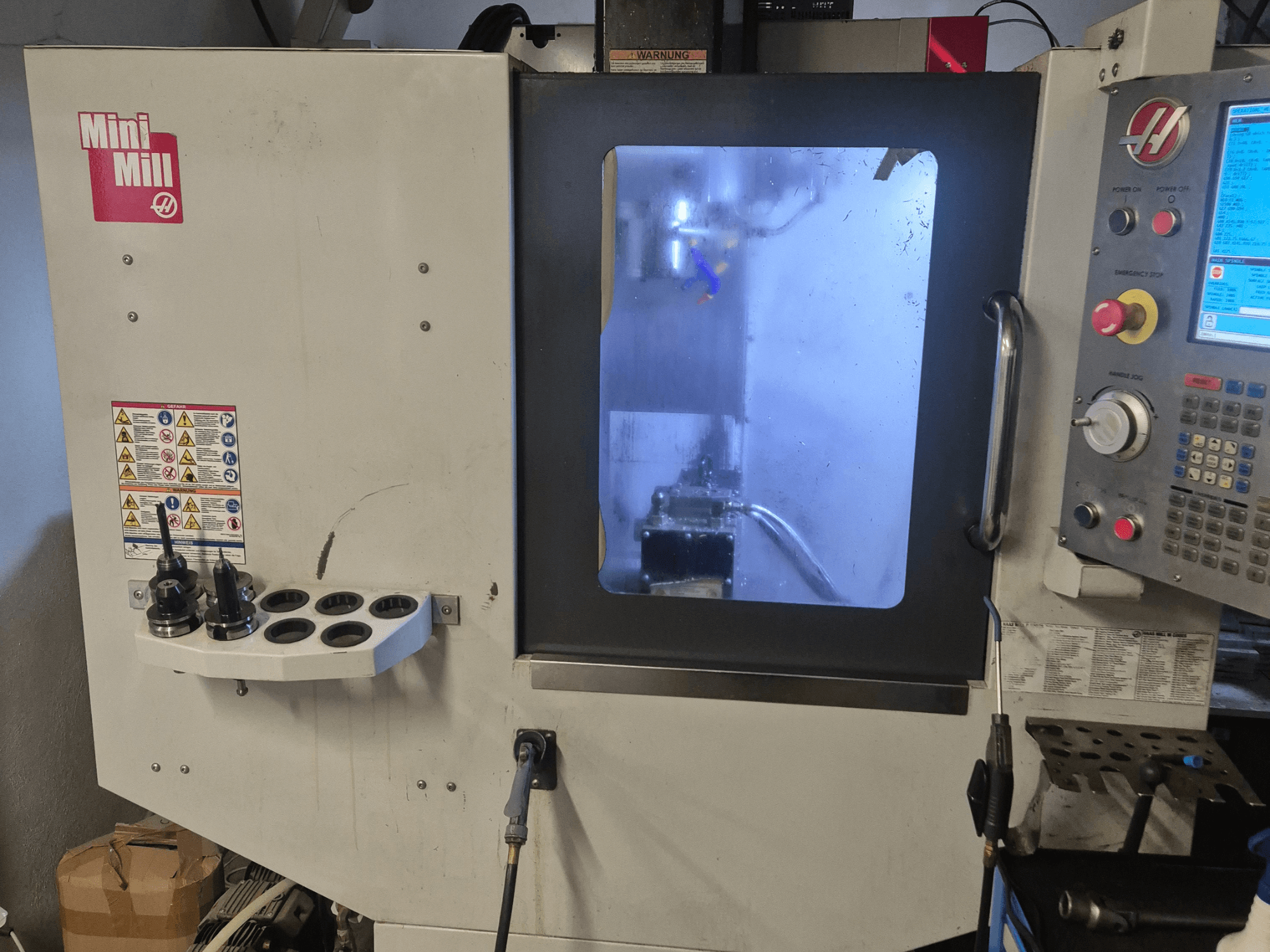 HAAS Mini Freze'nin önden görünümü, kontrol paneli, takım tutucular ve soğutma sıvısı ile işleme alanına bakış.