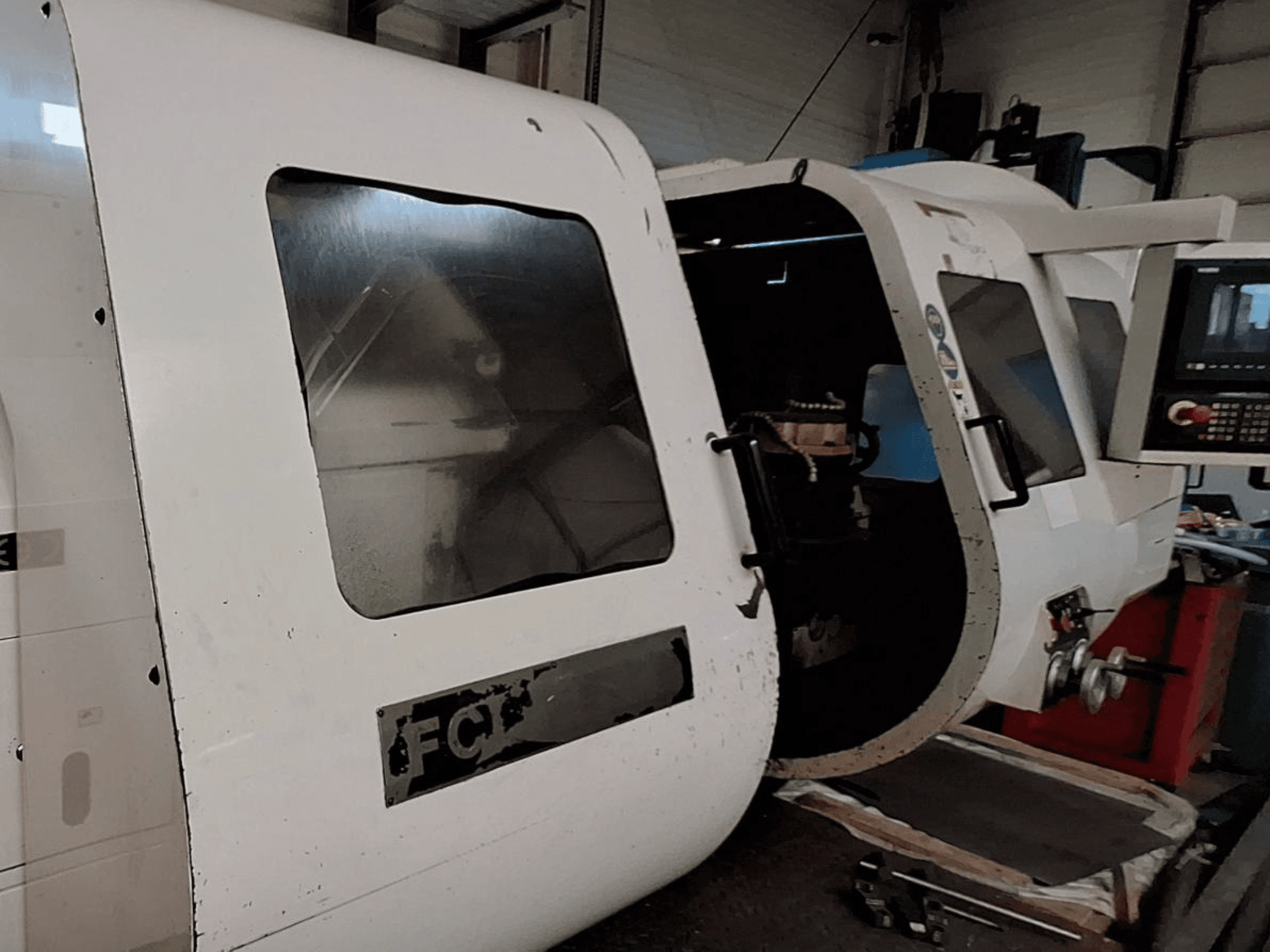 Görünür kontrol panelli ve açık kapılı, iç bileşenleri sergileyen beyaz CNC makinesi; önden görünüm. Marka: FCT.