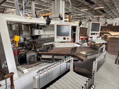 Çift monitörlü ve kontrol panelli IMA hassas ahşap işleme makinesi, konveyör ve takım alanını gösteren önden görünüm.