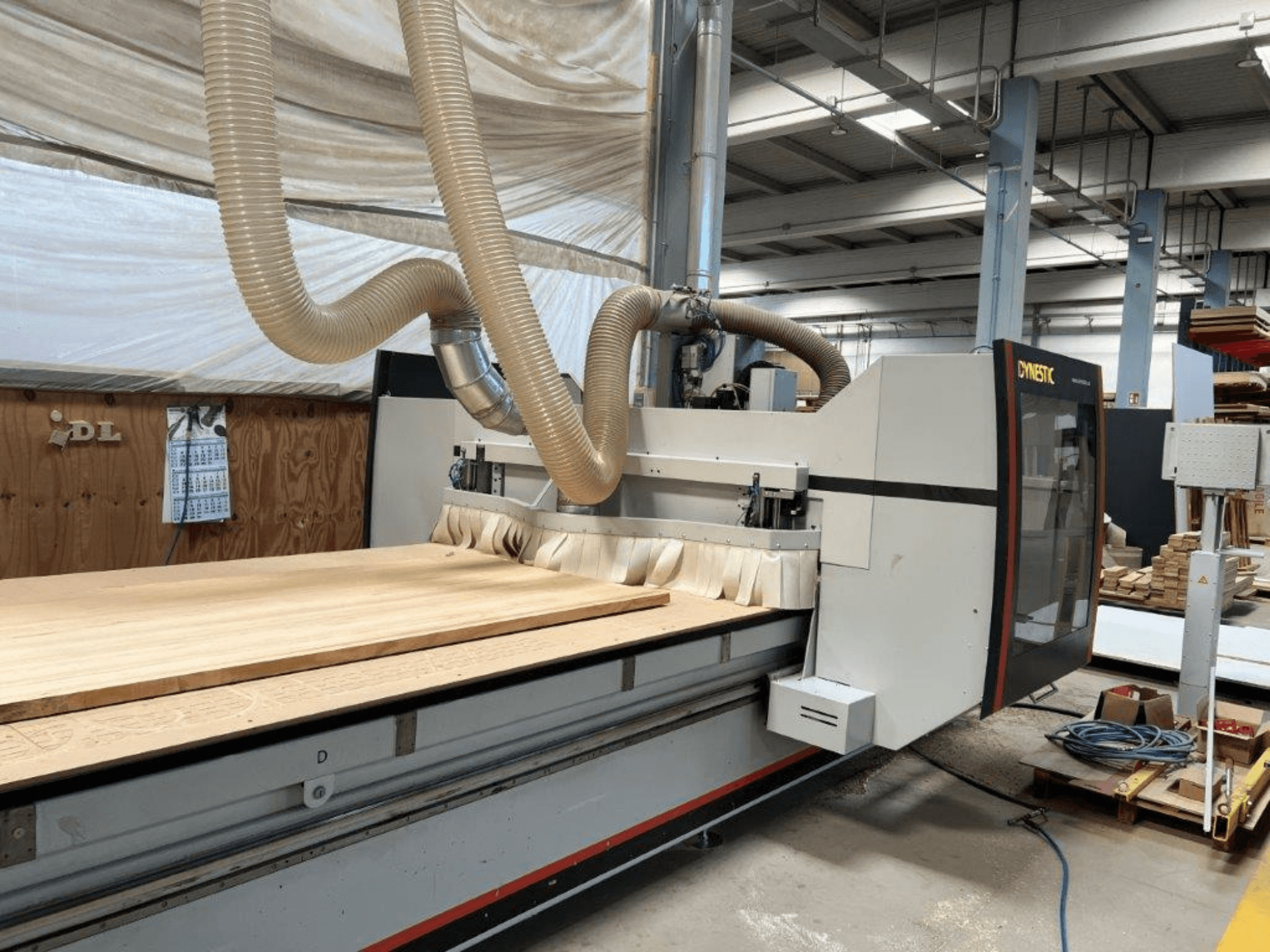 Dynestic CNC makinesi, önden görünüm, atölye ortamında büyük bir ahşap iş parçası ve toz emme hortumu.