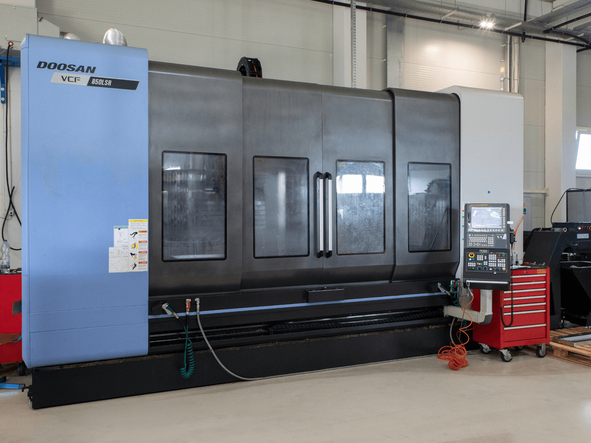 DOOSAN VCF850 Freze-Tornalama Merkezi, önden görünüm; geniş çift pencereler, kontrol paneli ve takım saklama bölmesi ile donatılmıştır. İşleme için idealdir.