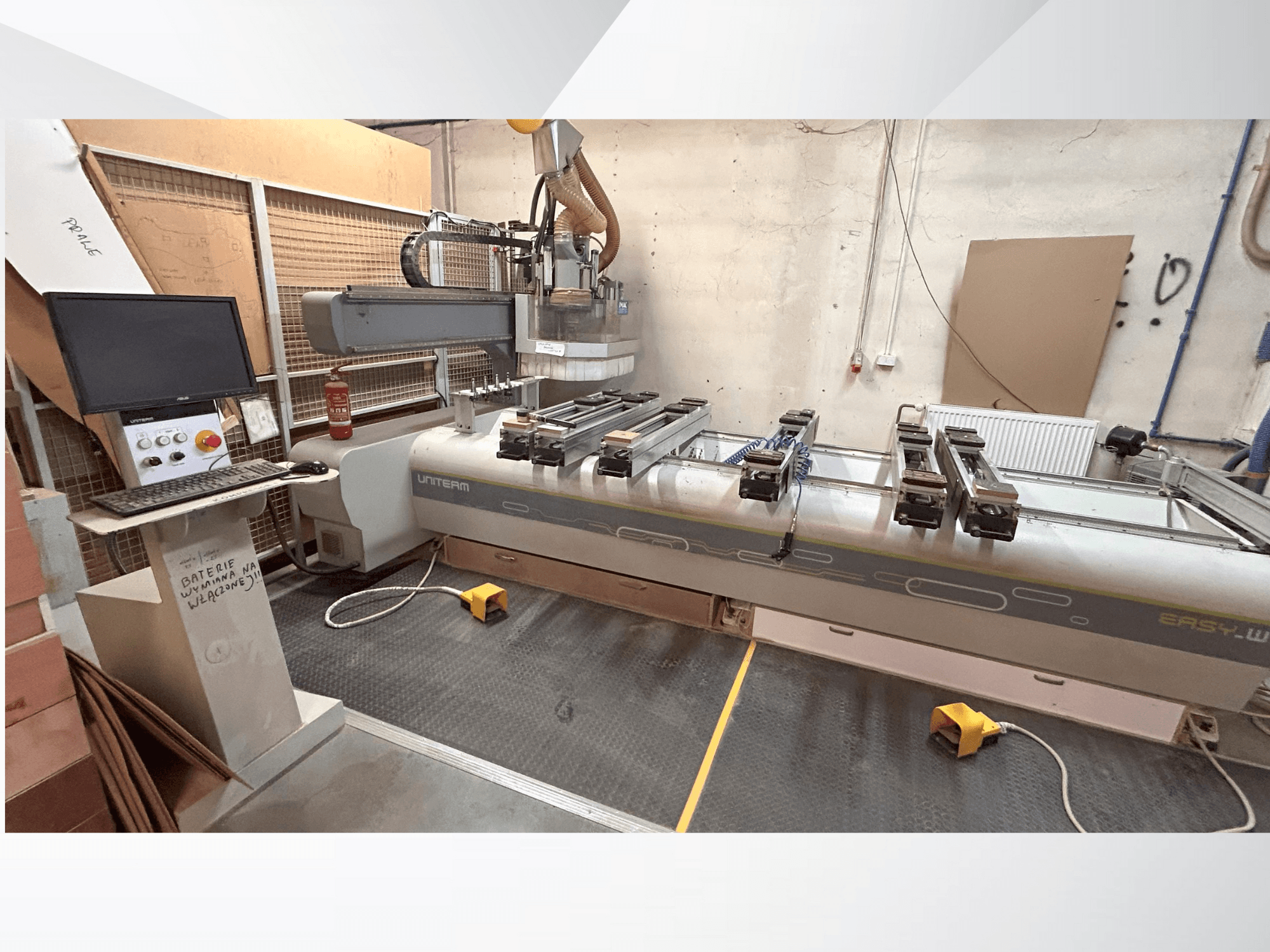 Bir UNITEM EASY-W CNC makinesinin önden görünümü, kontrol paneli, monitör ve çalışma masasında kelepçeli iş parçaları.