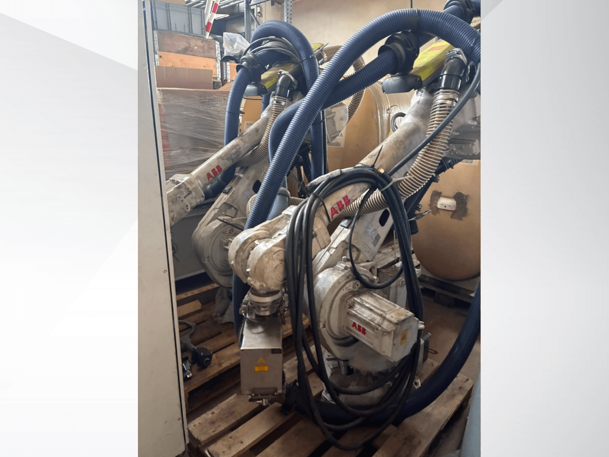 ABB IRB 4600-40/2.55 robot kolu; çift kol ve bağlı hortumları gösteren yan görünüm; bir depo ortamında paletlerin üzerine monte edilmiş.