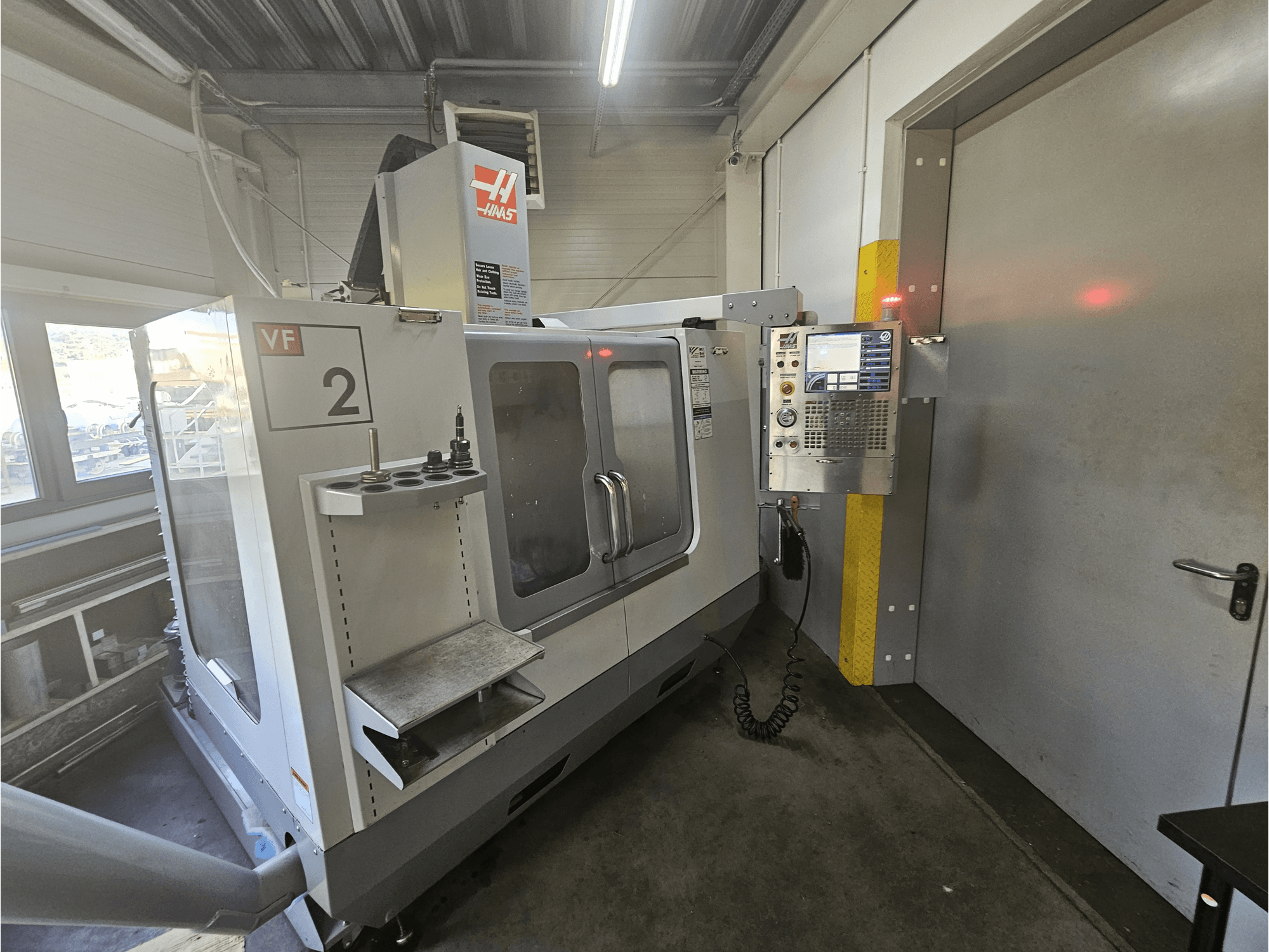 Haas VF-2 CNC freze makinesi, önden görünüm, kontrol panelini, takım tutucuları ve çalışma alanında açık bir pencereyi gösterir.