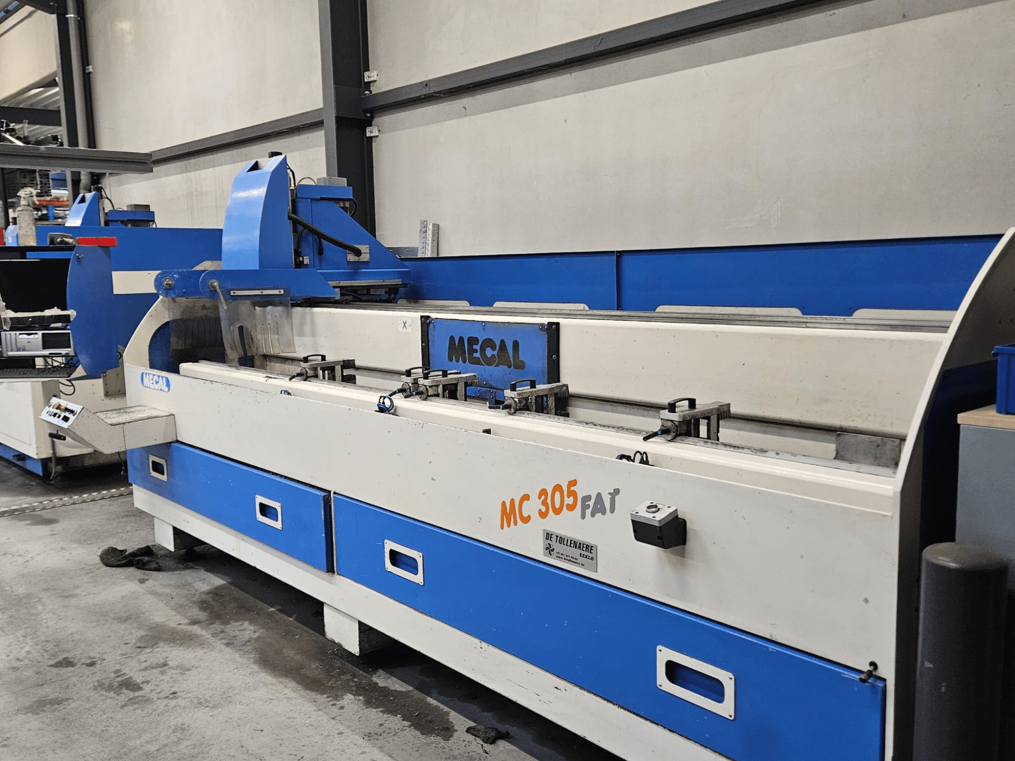 Fabrika ortamında MECAL MC 305 FAT makinesi, kontrolleri ve mavi beyaz tasarımı sergileyen önden görünüm.