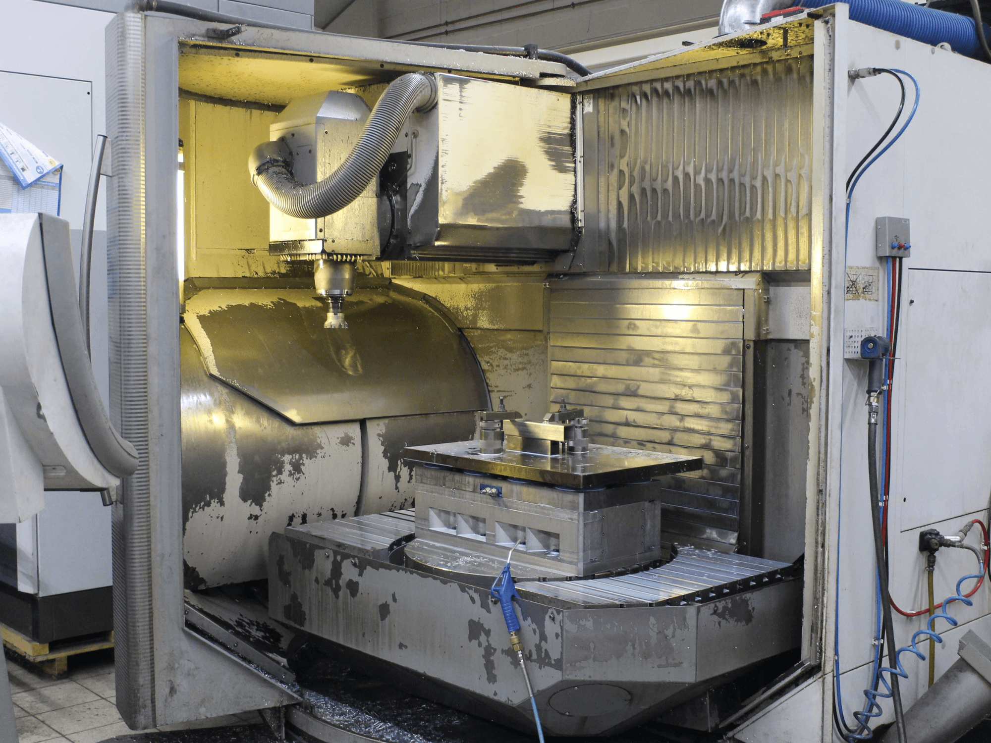CNC freze makinesinin içi, yandan görünüm, metal talaşı ve soğutma sıvısı kalıntısı ile iş parçasını ve kesici takımı gösterir.