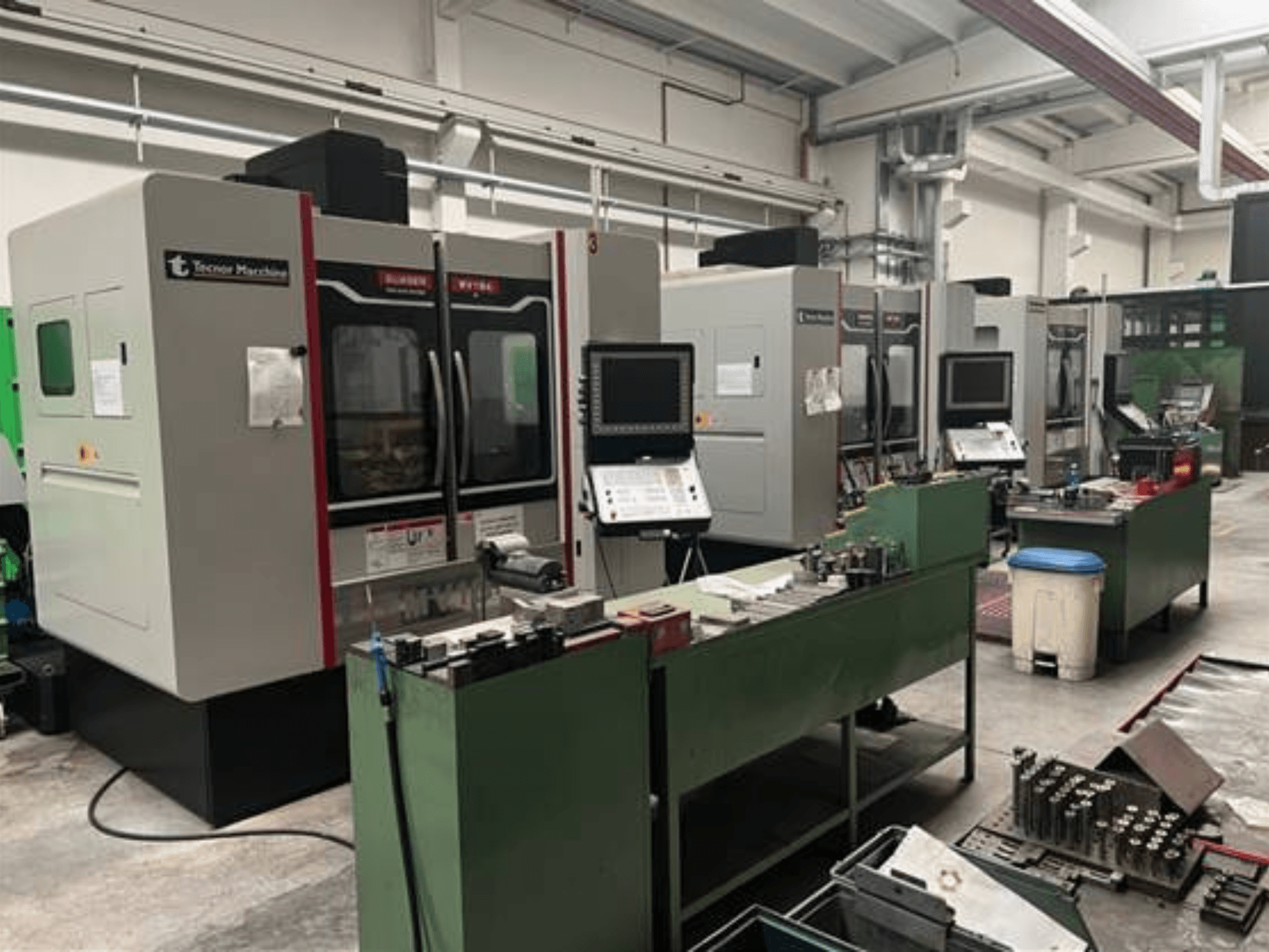 Bir atölyede Tecnoer Marchine'den dört CNC makinesi, önden görünüm, yeşil tezgahlarda aletler ve parçalar.