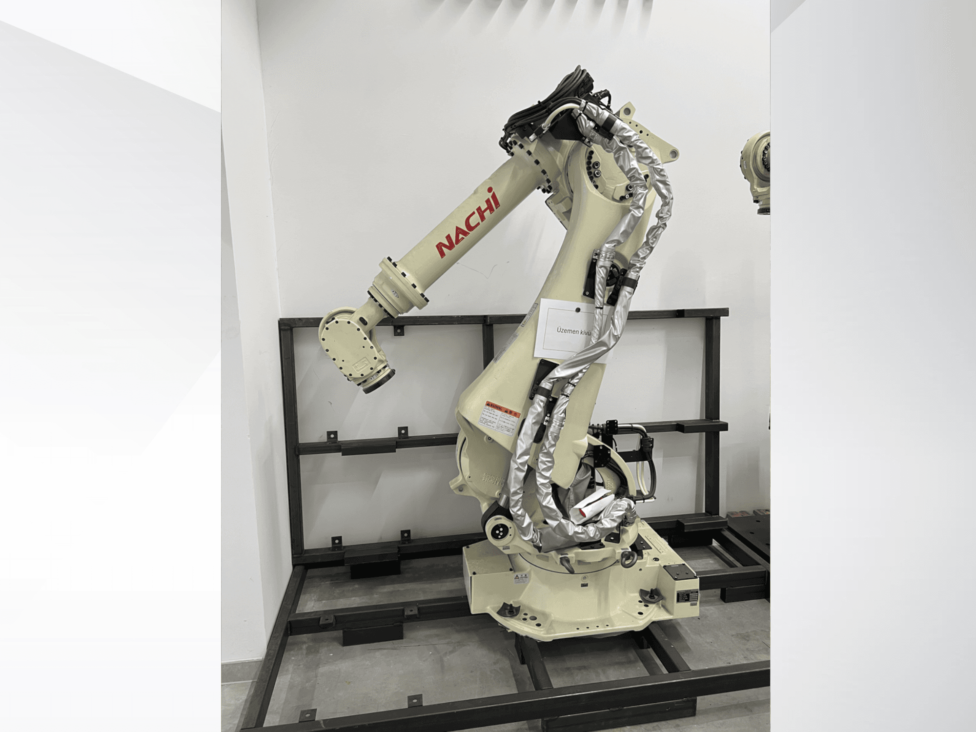 NACHI SRA166-01 robot kolu yandan görünümde, esnek mafsallara, bağlı kablolara sahiptir ve koruyucu bir çerçeve üzerine monte edilmiştir.