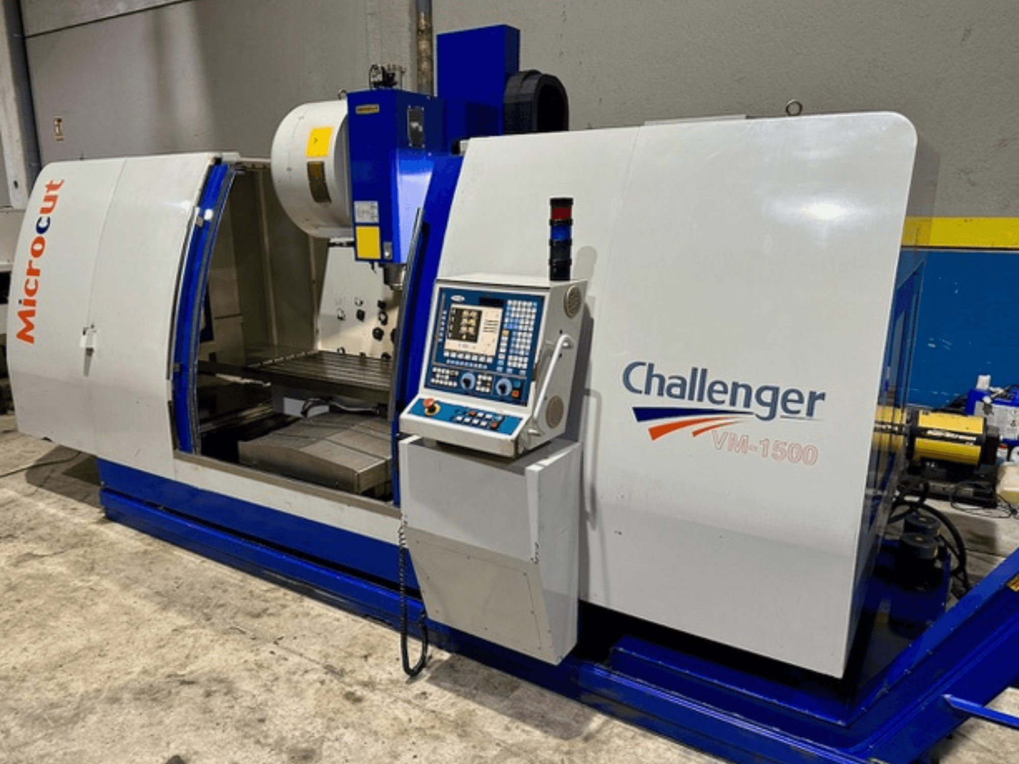 Microcut Challenger VM-1500 CNC makinesi, önden görünüm, kontrol paneli, çalışma alanı ve mavi bir tabana sahiptir.