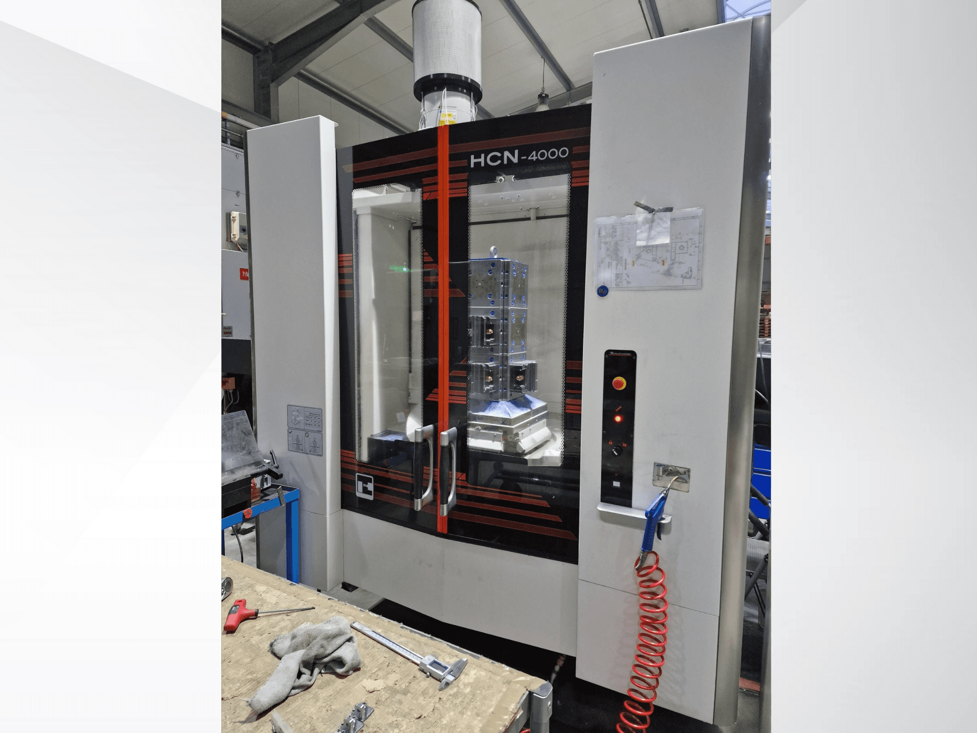 HCN-4000 CNC makinesinin önden görünümü, cam panel, düğmeli kontrol paneli ve ekli bir plan.