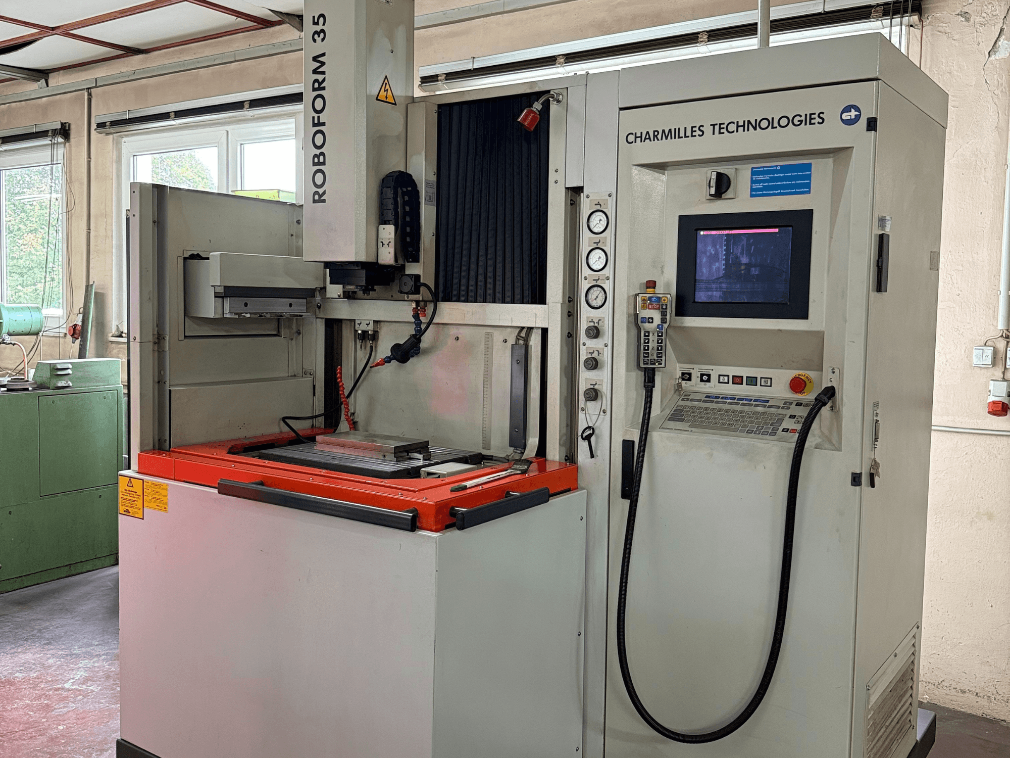 Charmilles Technologies Roboforn 35 makinesi, önden görünüm, kontrol panelini, monte edilmiş aletleri ve güvenlik etiketlerini gösterir.