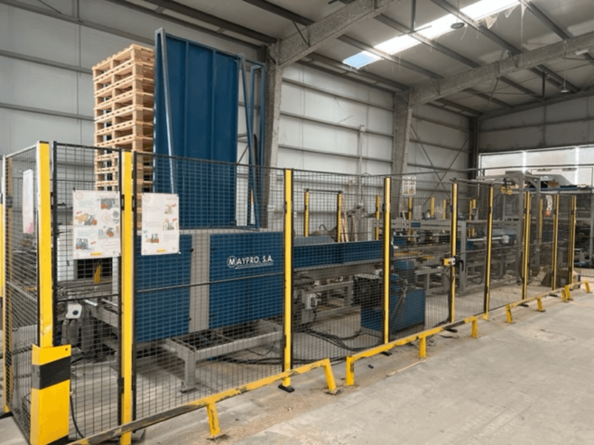 Maypro S.A.'nın bir depodaki endüstriyel palet paketleme makinesi, güvenlik ağı ve operasyonel kontroller, yandan görünüm.