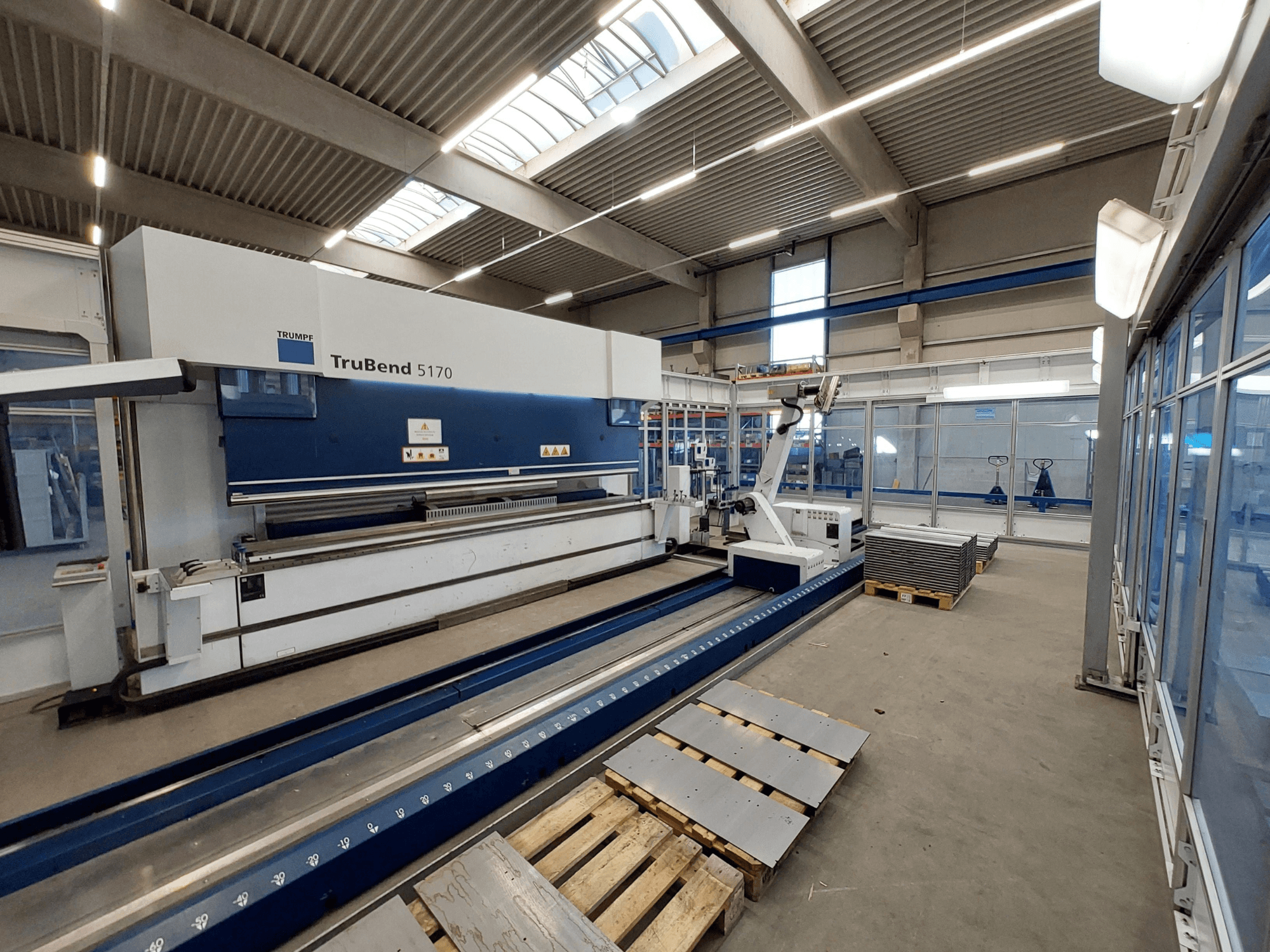 TRUMPF TruBend 5170 abkant pres, atölyede, yandan görünüm, bükme takımını ve paletler üzerinde istiflenmiş sacları gösteriyor.