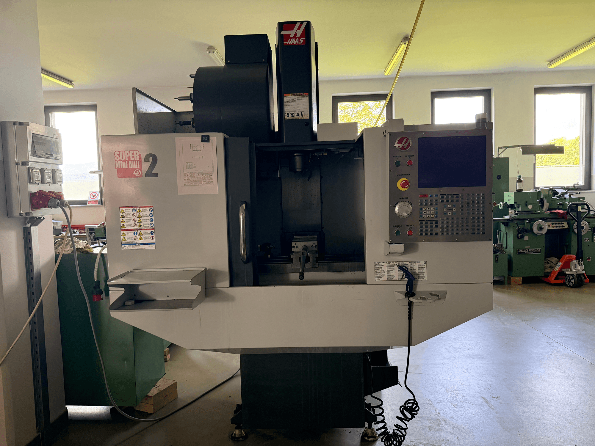 Haas Mini Mill 2 dikey işleme merkezinin önden görünümü, kontrol paneli ve uyarı etiketli takım alanı.