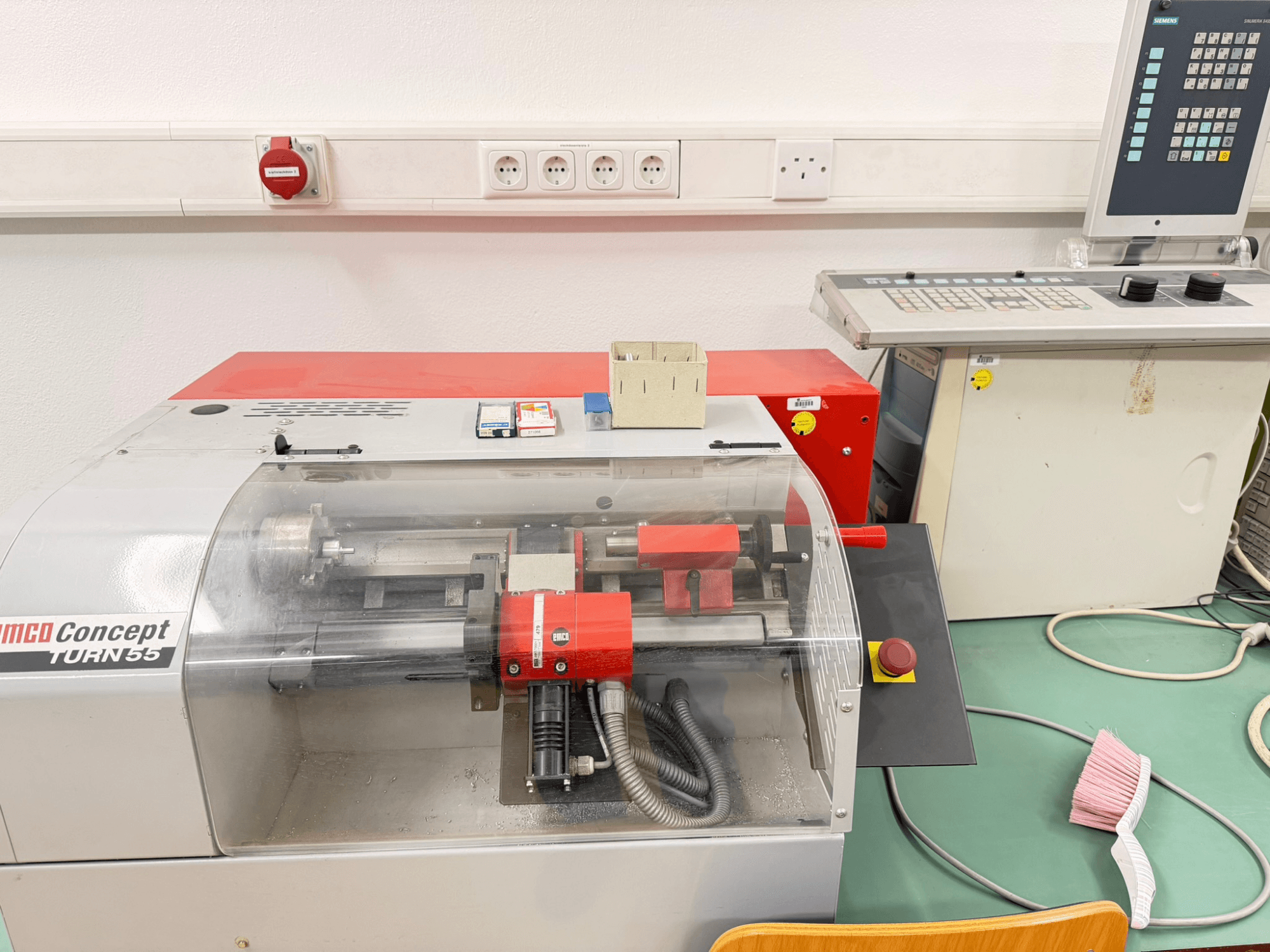 Kırmızı ve gri dış yüzeyli EMCO Concept Turn 55 yatay tornalama makinesi, kontrolleri ve çalışma alanını gösteren önden görünüm.
