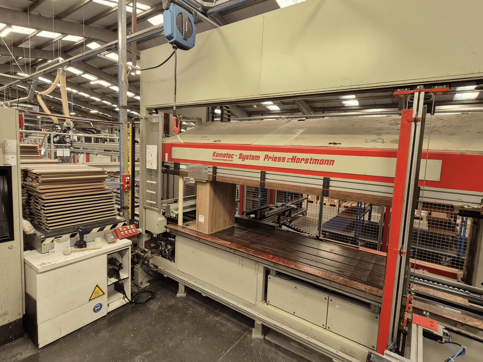 PREISS U HORTSTMANN tarafından üretilen kaplama presi KP-5-CNC, önden görünüm, istiflenmiş kaplama levhaları ve kontrol paneli.