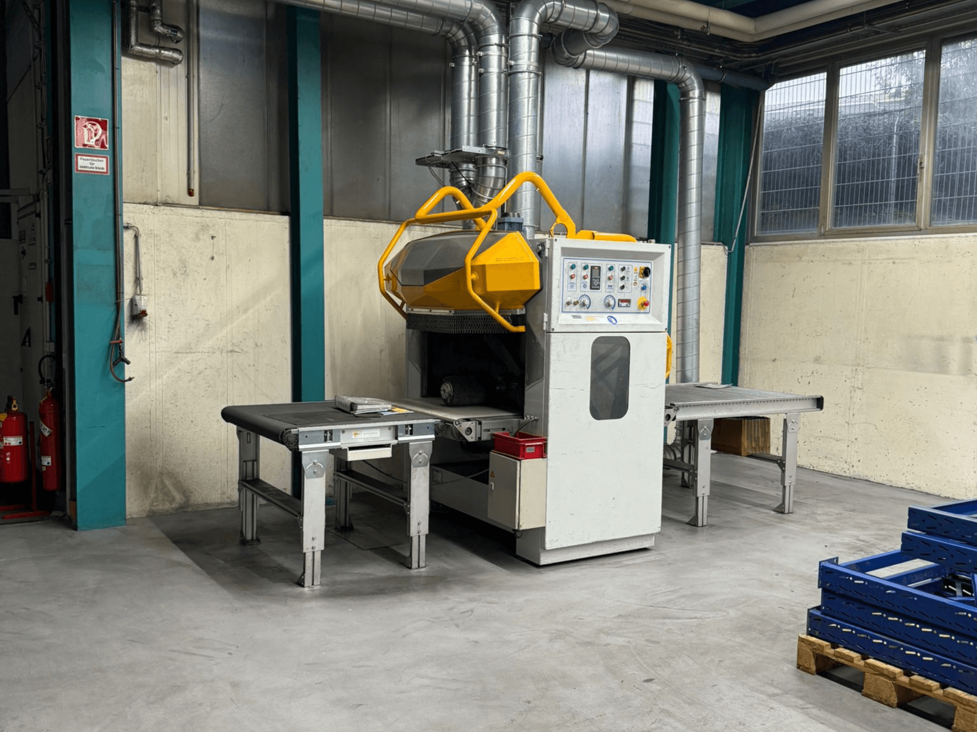 Çapak alma makinesi Fladder AUT-1000 VAC fabrika ortamında, kontrol paneli, sarı güvenlik koruması ve bitişik çalışma masaları ile birlikte.