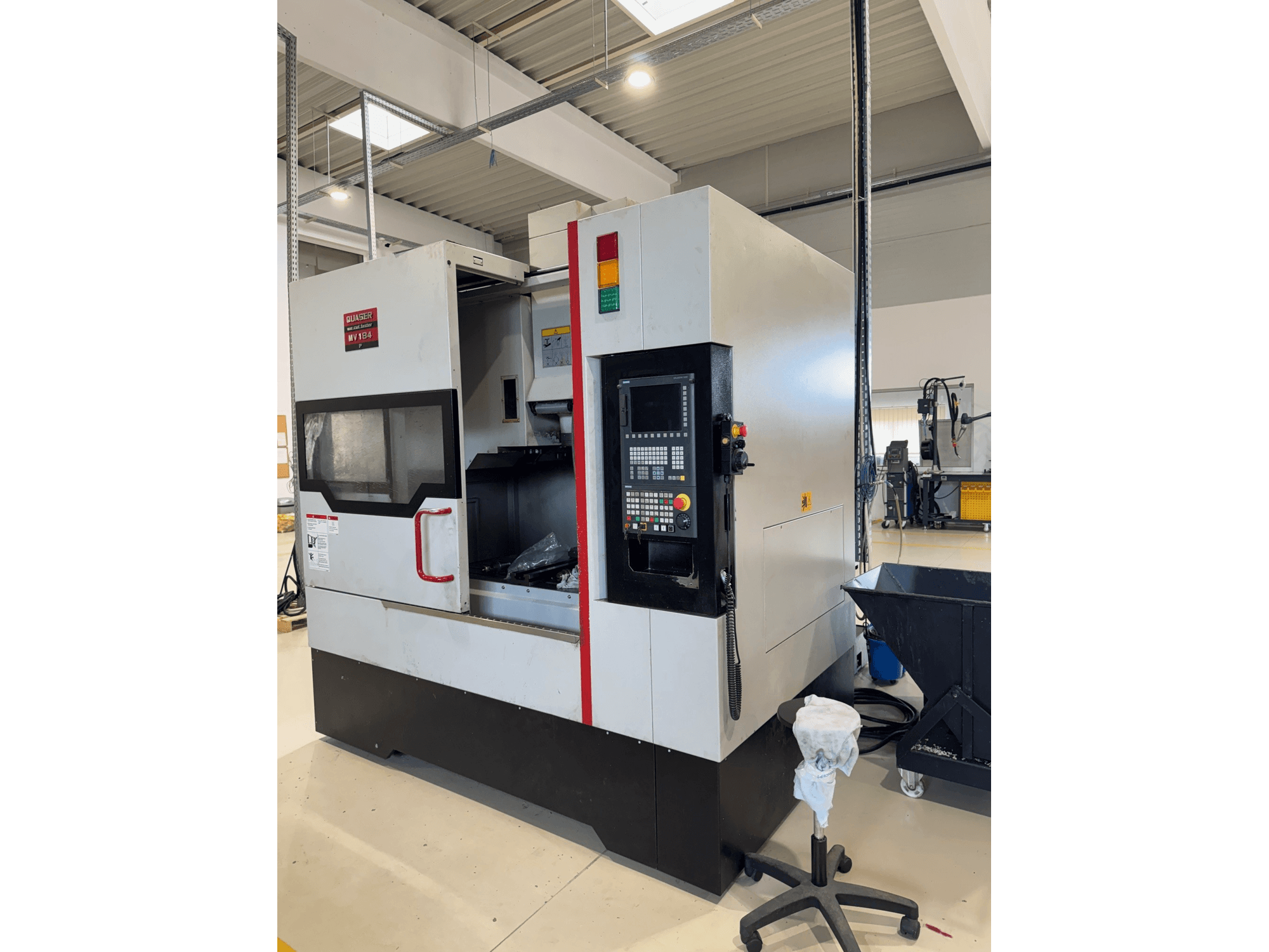 Quaser MV184P/12B dikey işleme merkezi, yandan görünüm; kontrol paneli ve işleme alanının görülebildiği açık ön kısım gösterilmektedir.