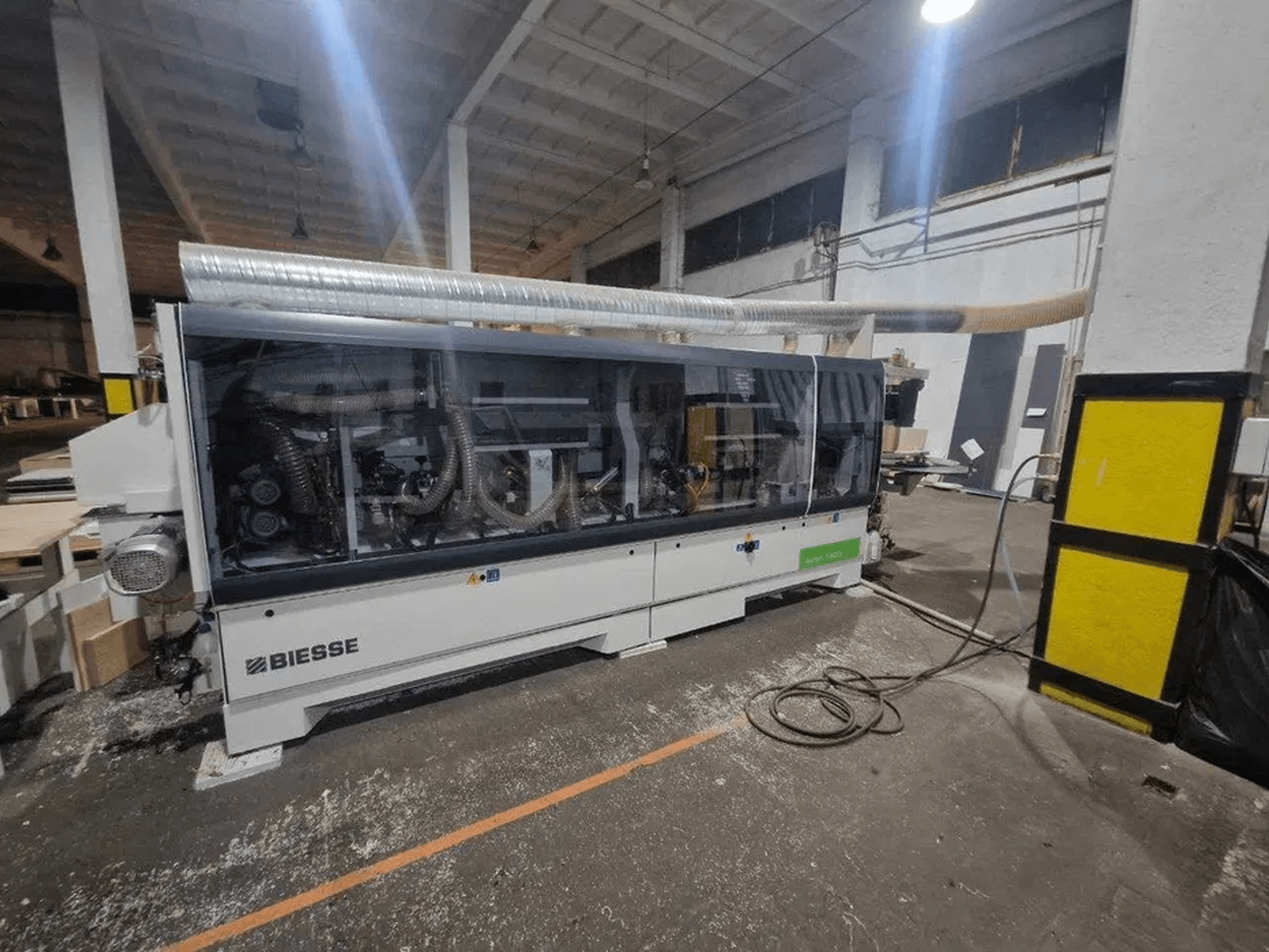 Bir atölyede bulunan, şeffaf bir kapağa ve görünür makine bileşenlerine sahip BIESSE Akron 1440 A kenar kaplama makinesi.