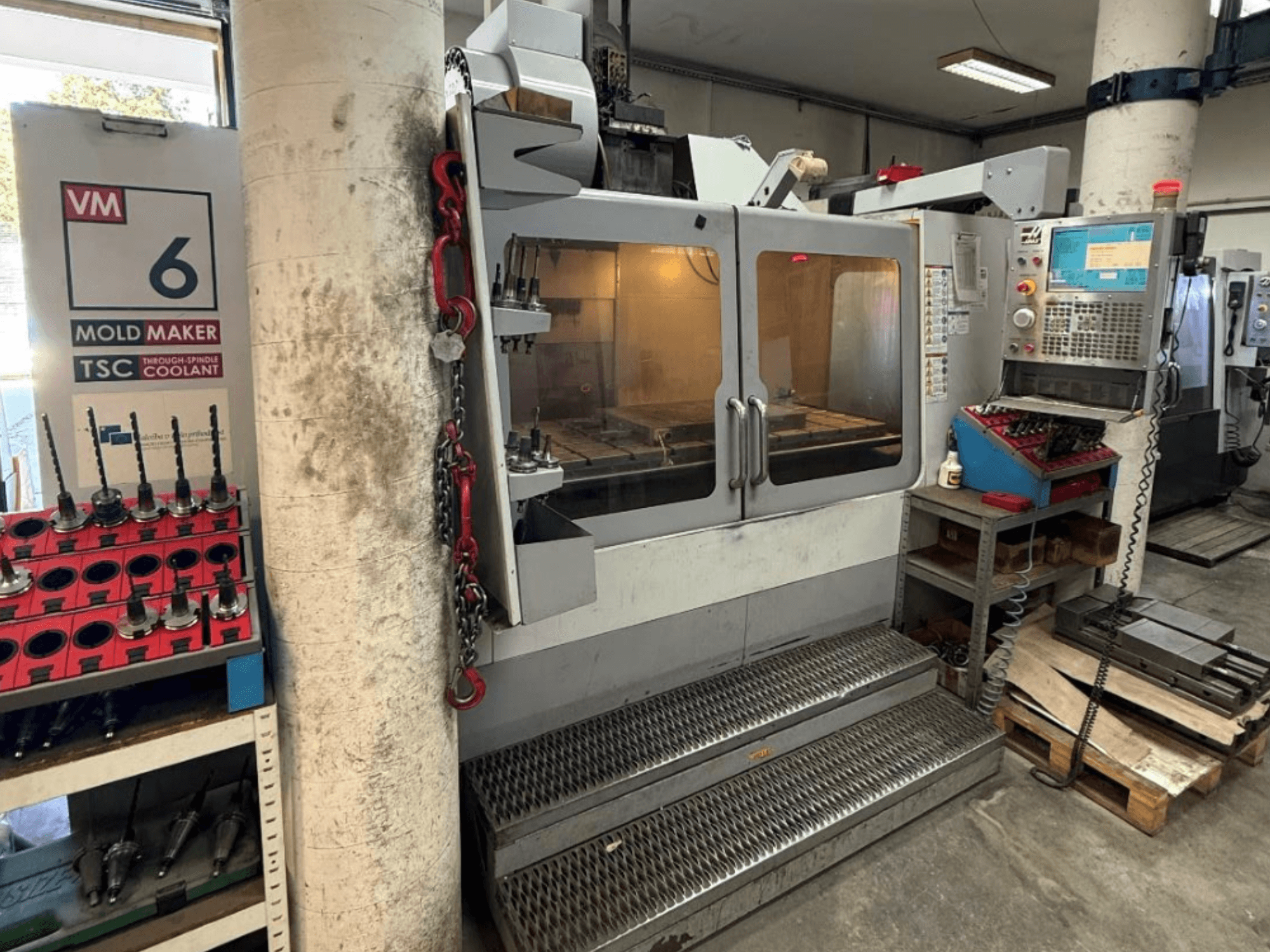 HAAS VM-6 HE dikey işleme merkezinin önden görünümü; kontrol paneli, soğutma sıvısı sistemi ve takım deposu görülebilir.