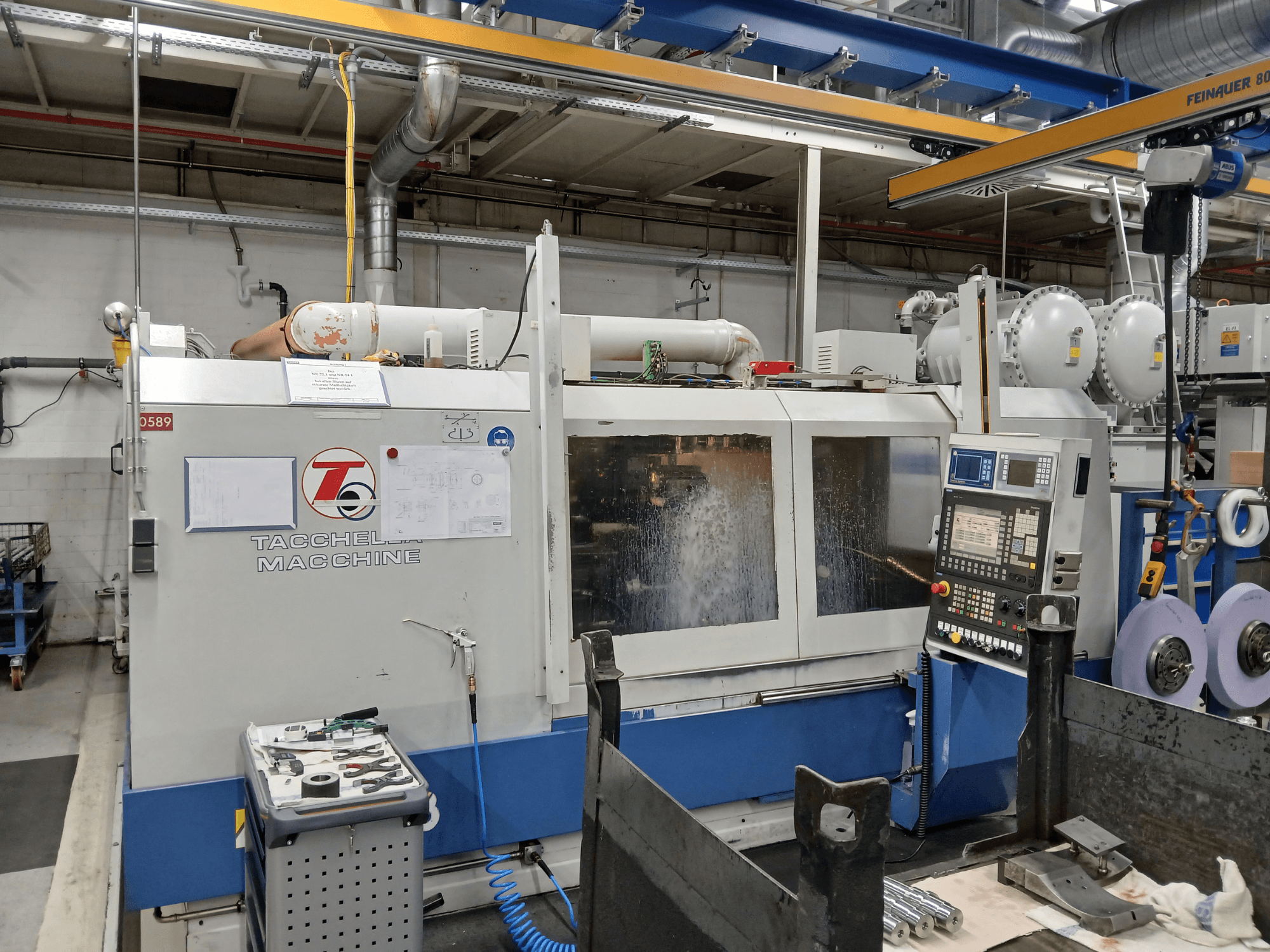 Tacchella işleme merkezinin önden görünümü, kontrol paneli ve takımlar görülebilir. Çalışma sırasında su soğutma sıvısı püskürür.