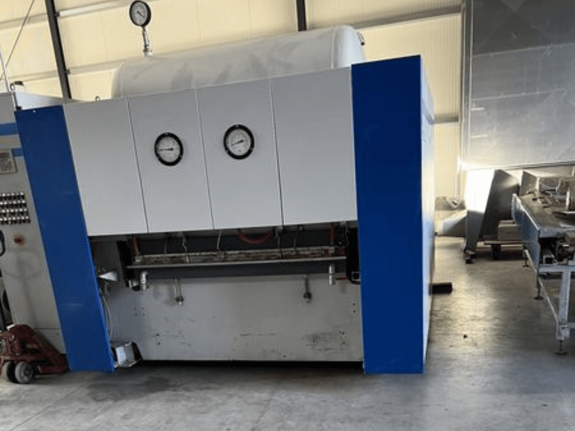 İki basınç göstergeli mavi ve beyaz endüstriyel makine, önden görünüm, bir kontrol paneli ve bitişik ekipman.