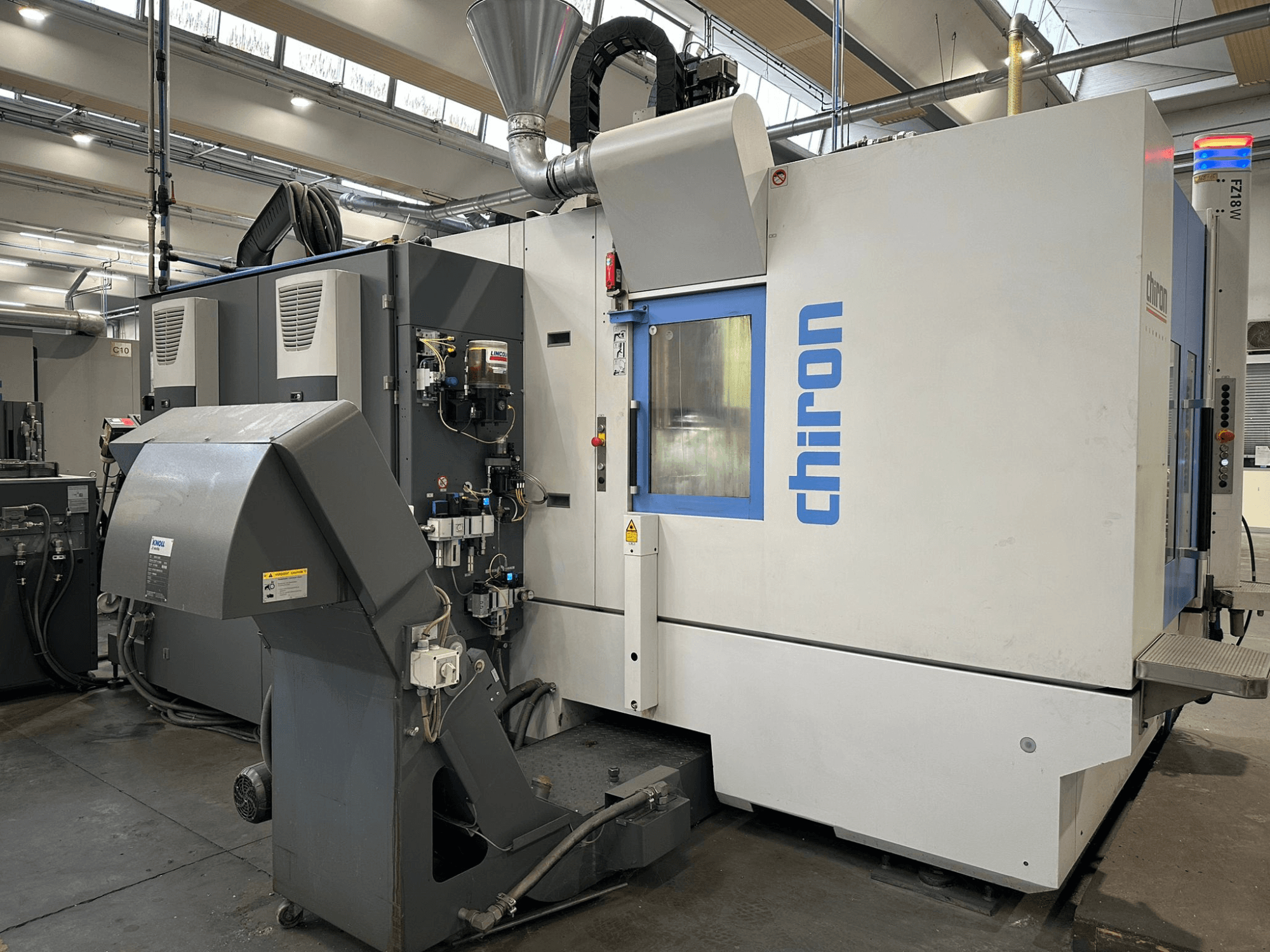 Gri ve beyaz Chiron CNC makinesi, önden görünüm, kontroller, borular ve toz emme başlığı.