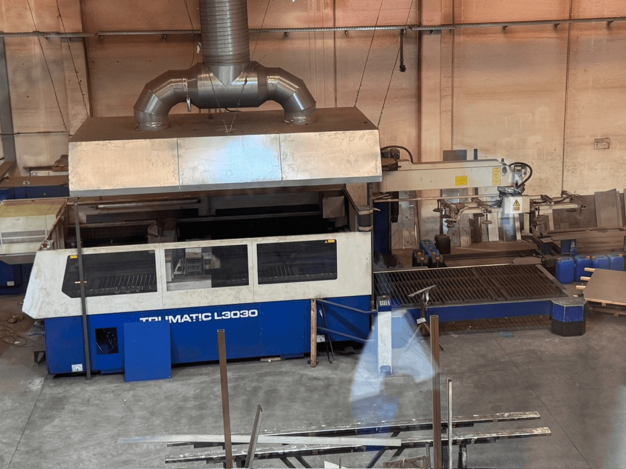 Bir atölyede bulunan CO₂ lazer kesim makinesi TRUMPF TRUMATIC L3030; kontrol paneli ve kesim yatağını gösteren önden görünüm.