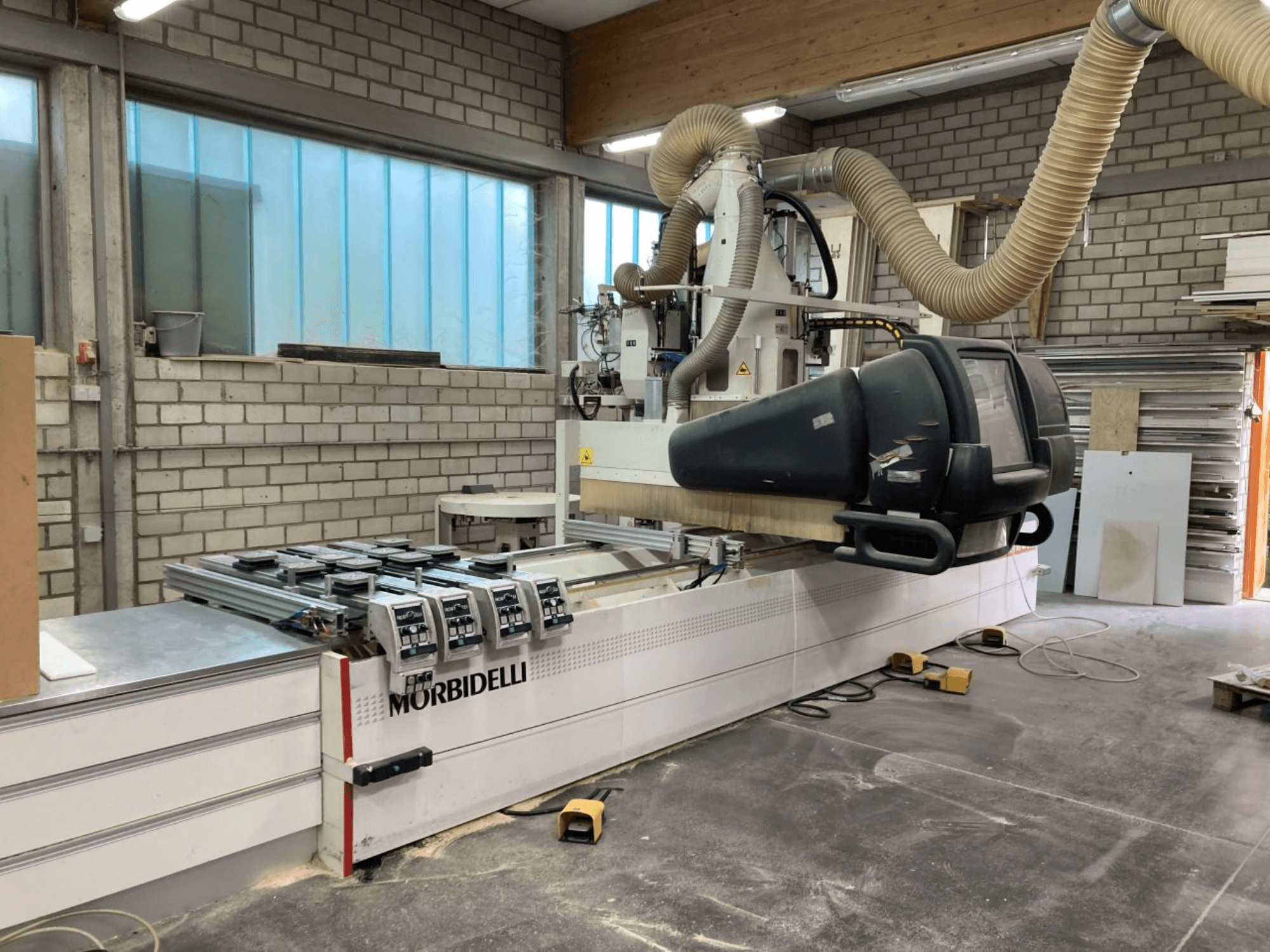 Bir atölyede MORBIDELLI CNC makinesi, kontrol paneli, toz emme sistemi ve yerleştirilmiş ahşap parça ile önden görünüm.