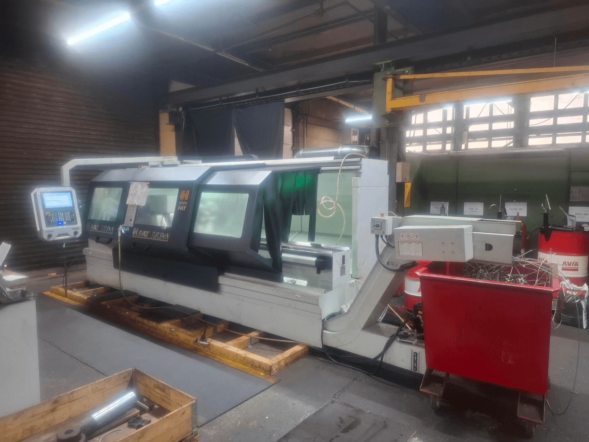 Bir atölyede ahşap paletler üzerine yerleştirilmiş, kontrol panelli bir FAT Tursan CNC makinesinin önden görünümü.