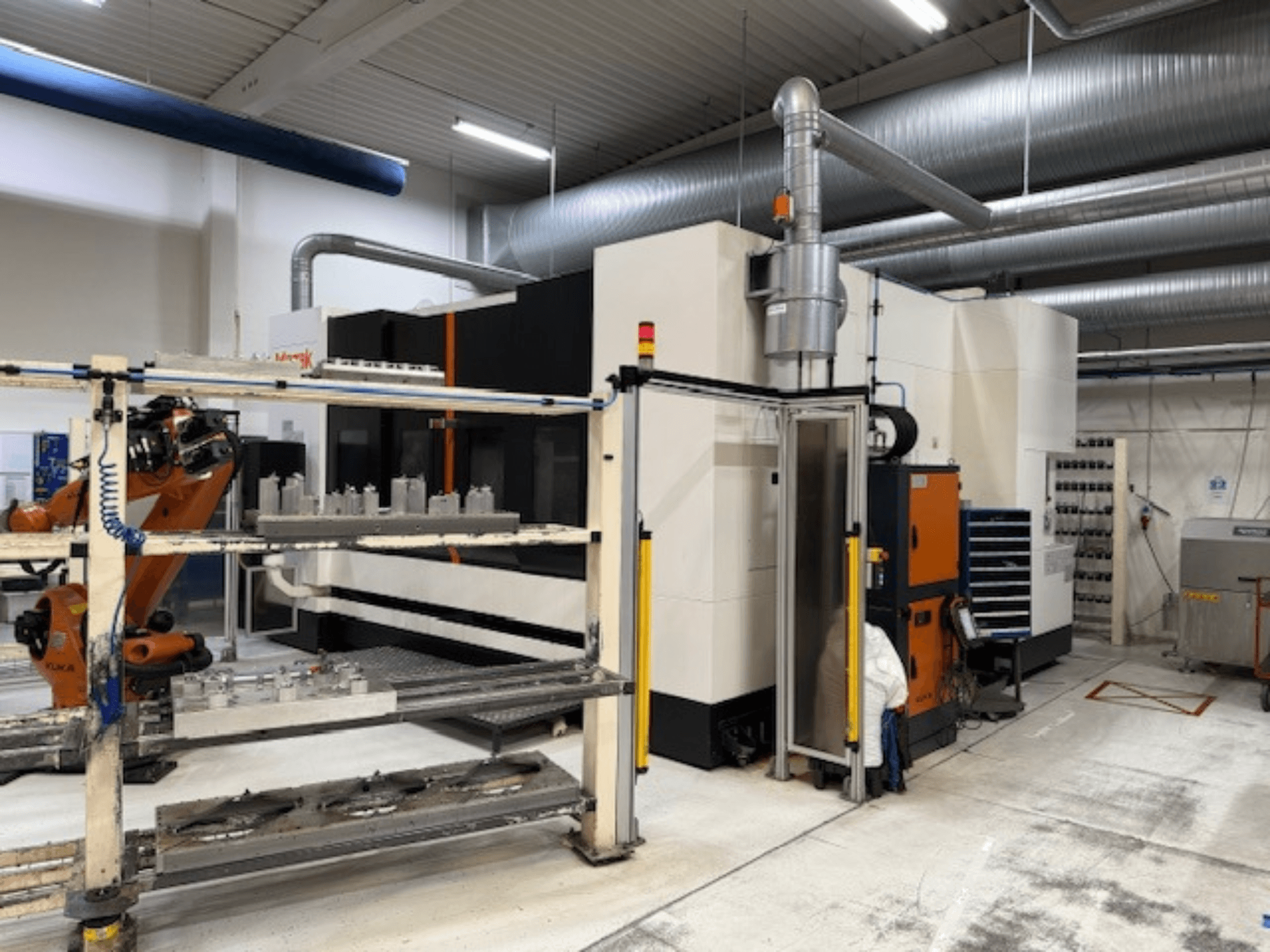 Robotik kollu ve güvenlik bariyerli endüstriyel CNC makinesi, havadar bir çalışma alanındaki kurulumun önden görünümünü içeriyor.
