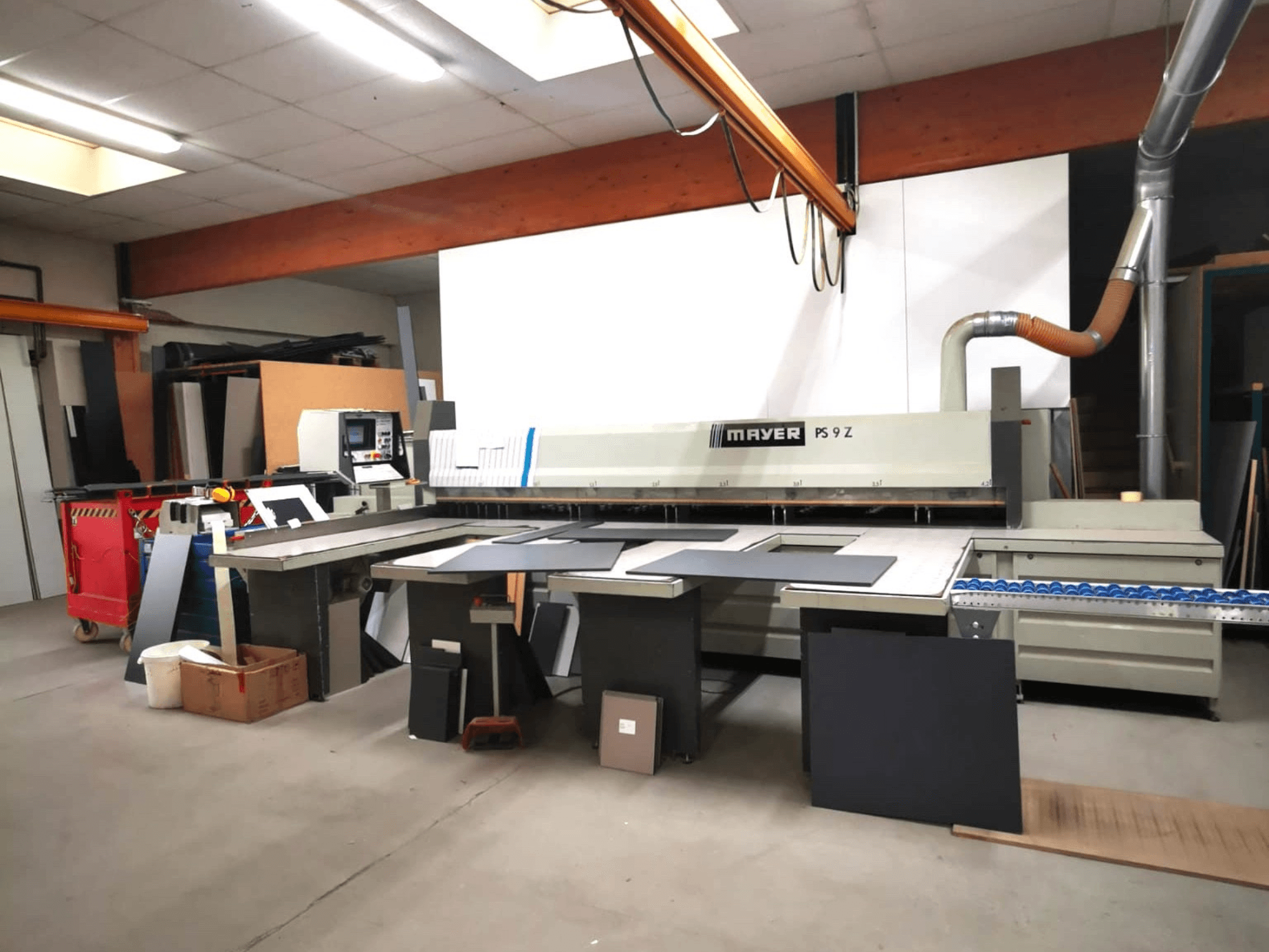 MAYER PS9 Z kesme makinesi bir atölyede, önden görünüm, çeşitli malzemeler ve bir konveyör sistemi görülebilir.