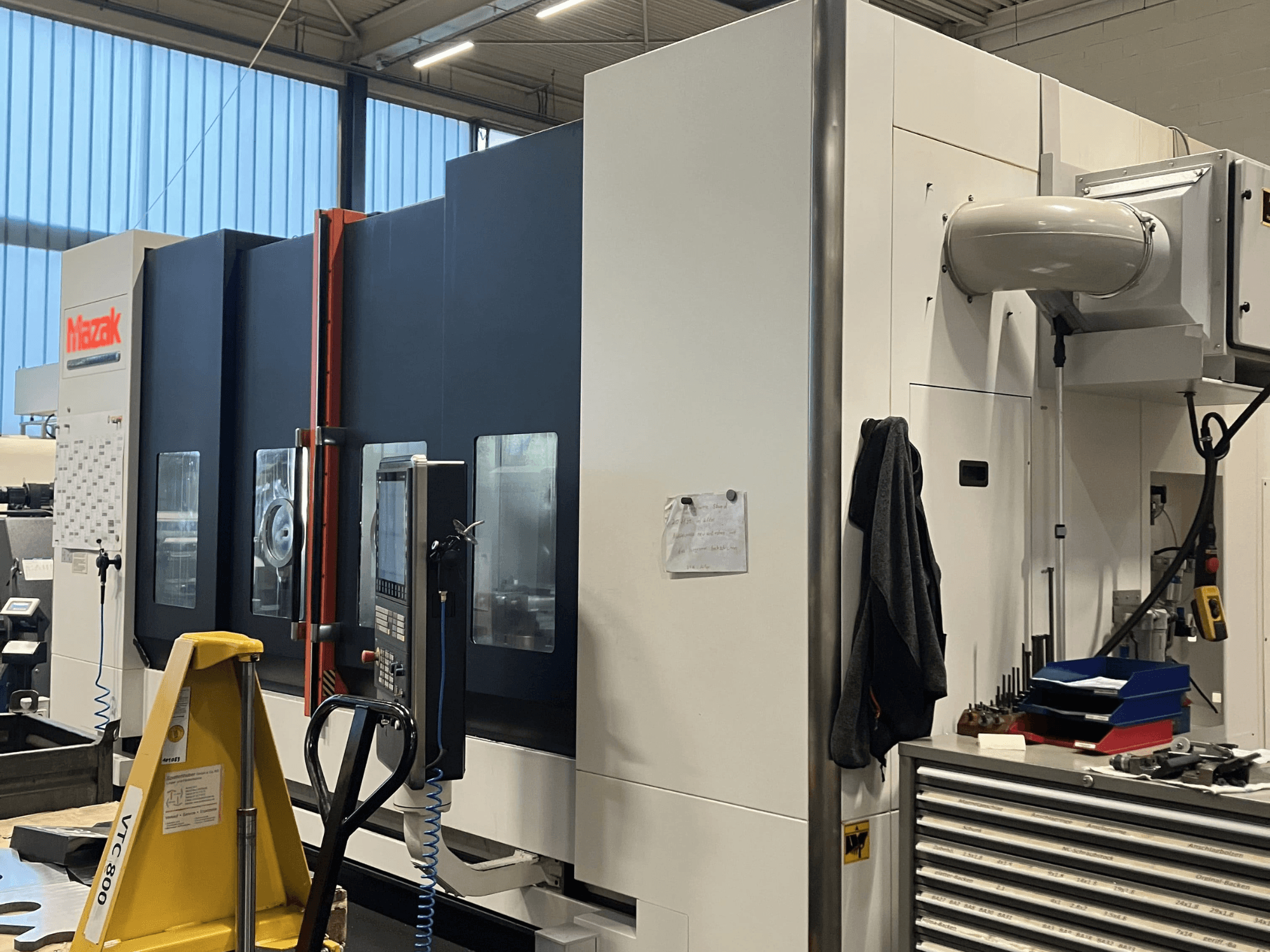 Bir atölye ortamında kontrol panelini ve güvenlik özelliklerini sergileyen Mazak CNC makinesi yandan görüntülenmiştir.